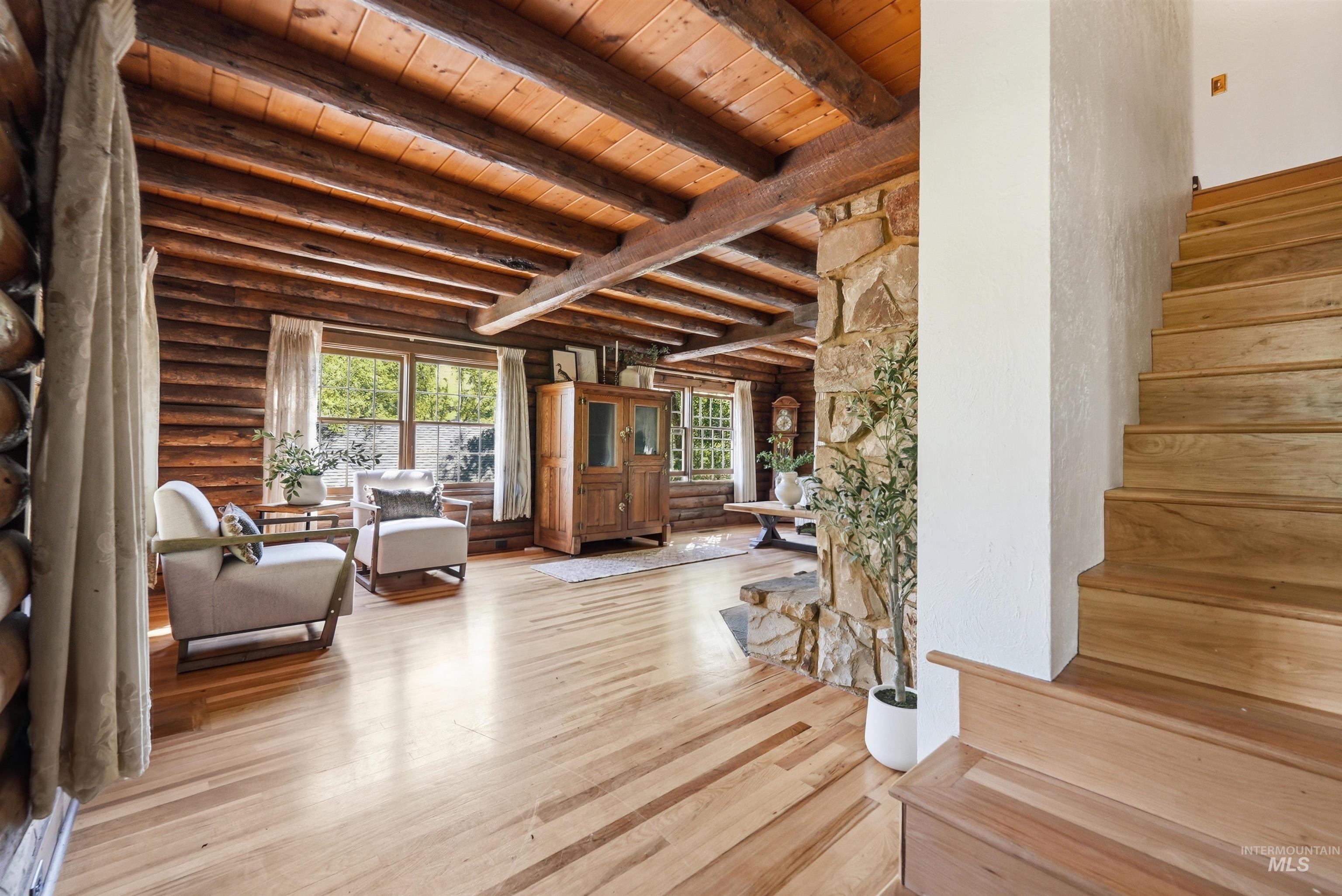 Expansive main floor living area showcasing wood flooring, exposed log walls, and a wood-beamed ceiling