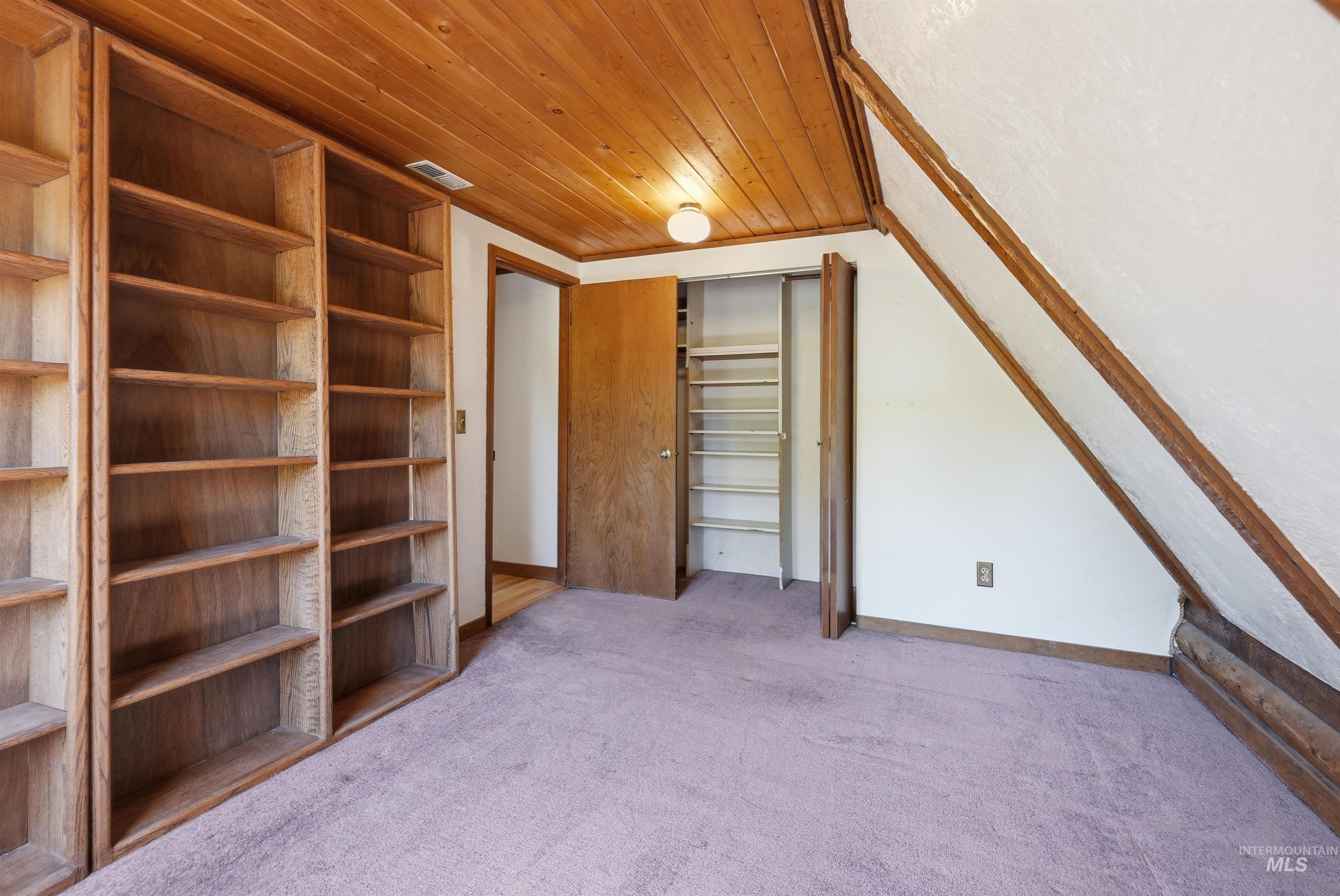 Built-in wood shelving units, wood-paneled ceiling, sloped ceiling detail, wood trim, and a built-in closet with shelving