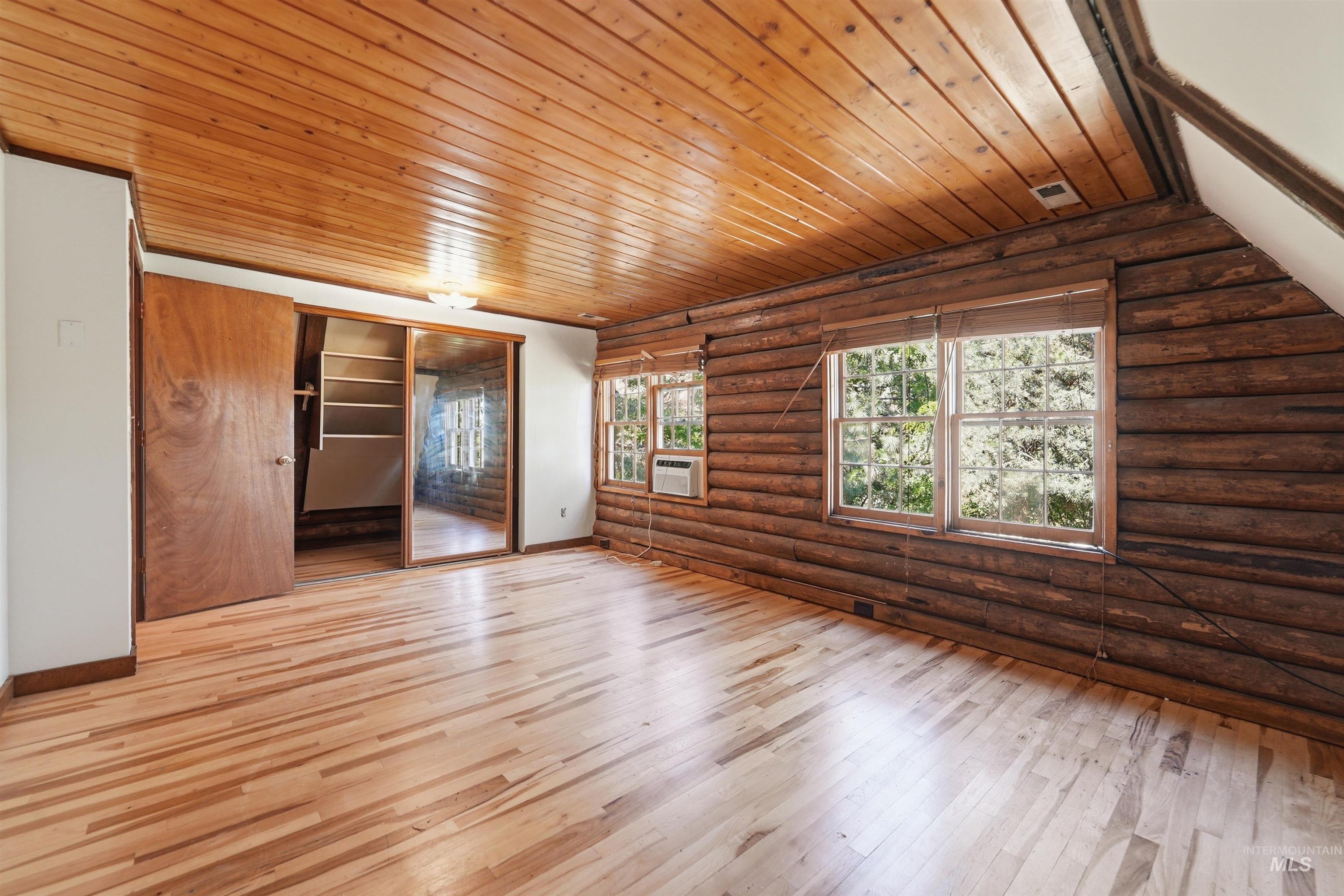 Spacious room featuring log wall construction, wood-finish flooring, and a wood-paneled ceiling