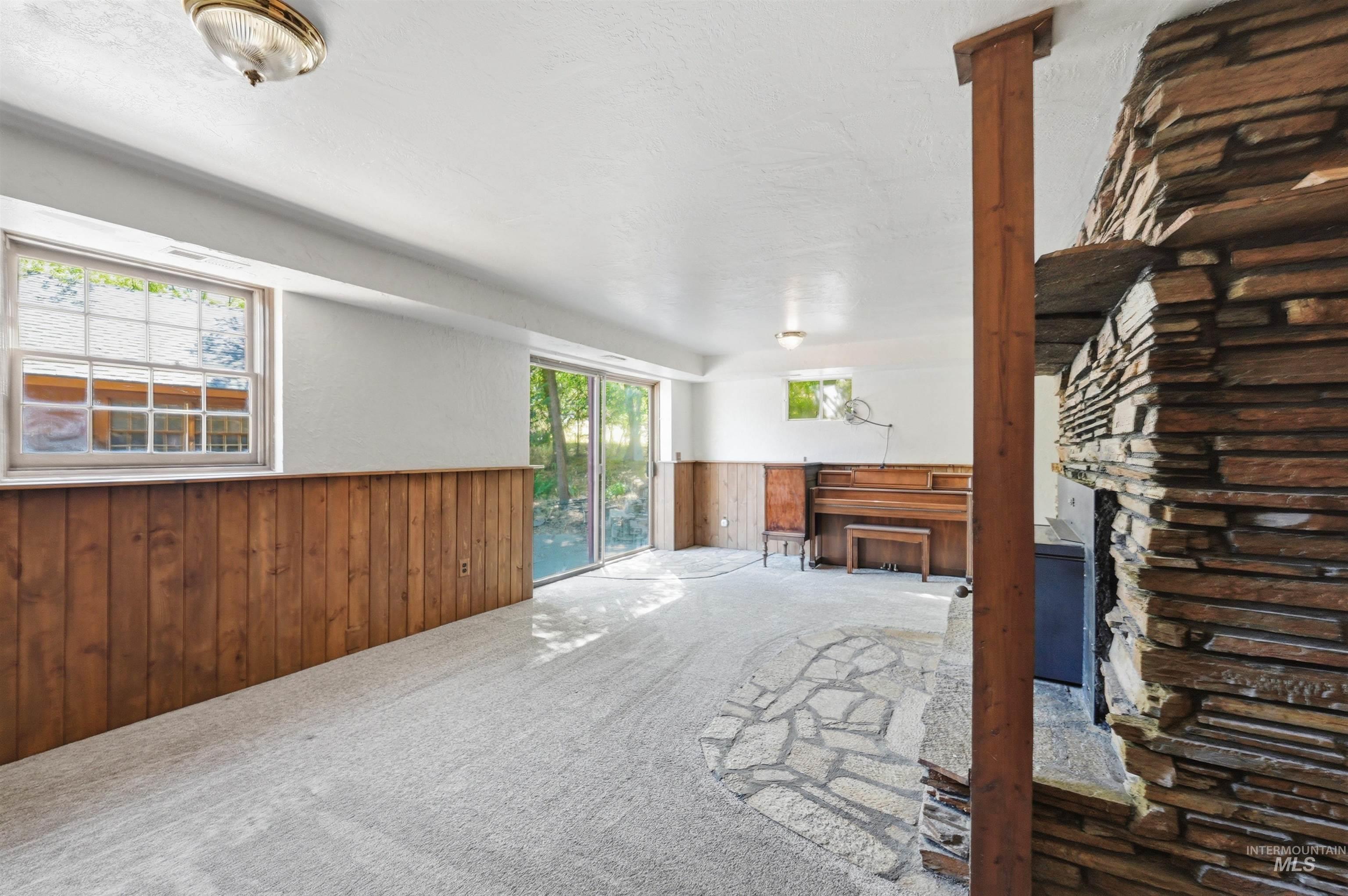 Spacious day light basement living room featuring a stone-clad fireplace and hearth, wood-finish wainscoting, and a ceiling-mounted light fixture