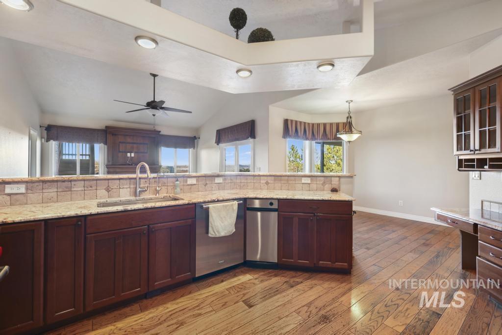 Kitchen featuring stainless steel dishwasher, light stone counters, dark brown cabinets, pendant lighting, and tasteful backsplash