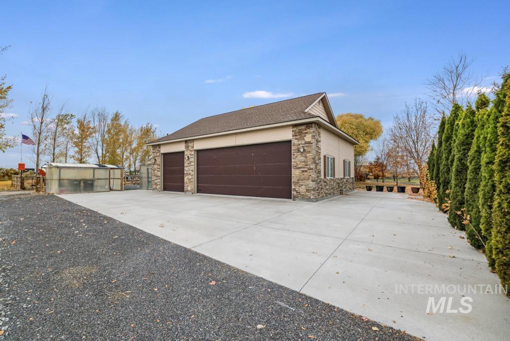 View of side of property with concrete driveway, an outdoor structure, stone siding, and a shingled roof