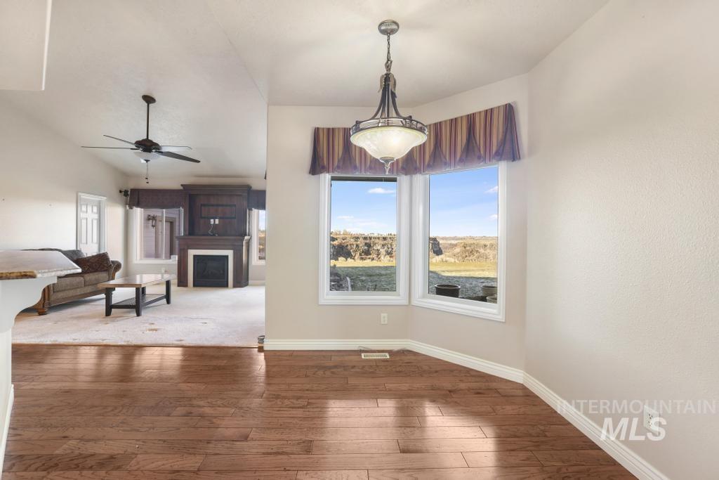 Unfurnished dining area featuring hardwood / wood-style floors, a fireplace, ceiling fan, and vaulted ceiling