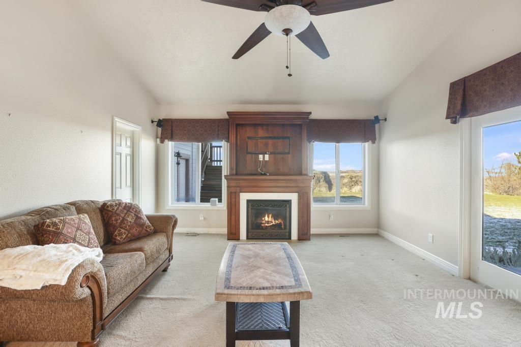 Living area with lofted ceiling, a warm lit fireplace, carpet floors, and ceiling fan