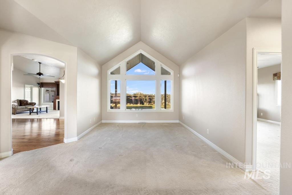 Unfurnished room featuring carpet, ceiling fan, lofted ceiling, a fireplace, and arched walkways