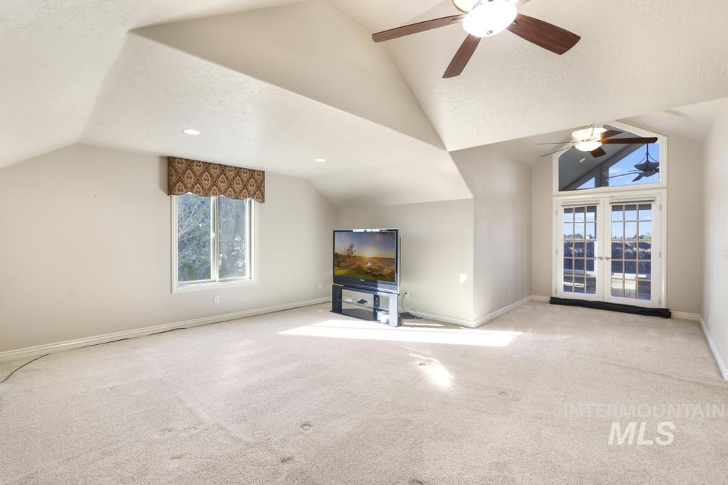 Unfurnished living room featuring lofted ceiling, carpet, a ceiling fan, and french doors