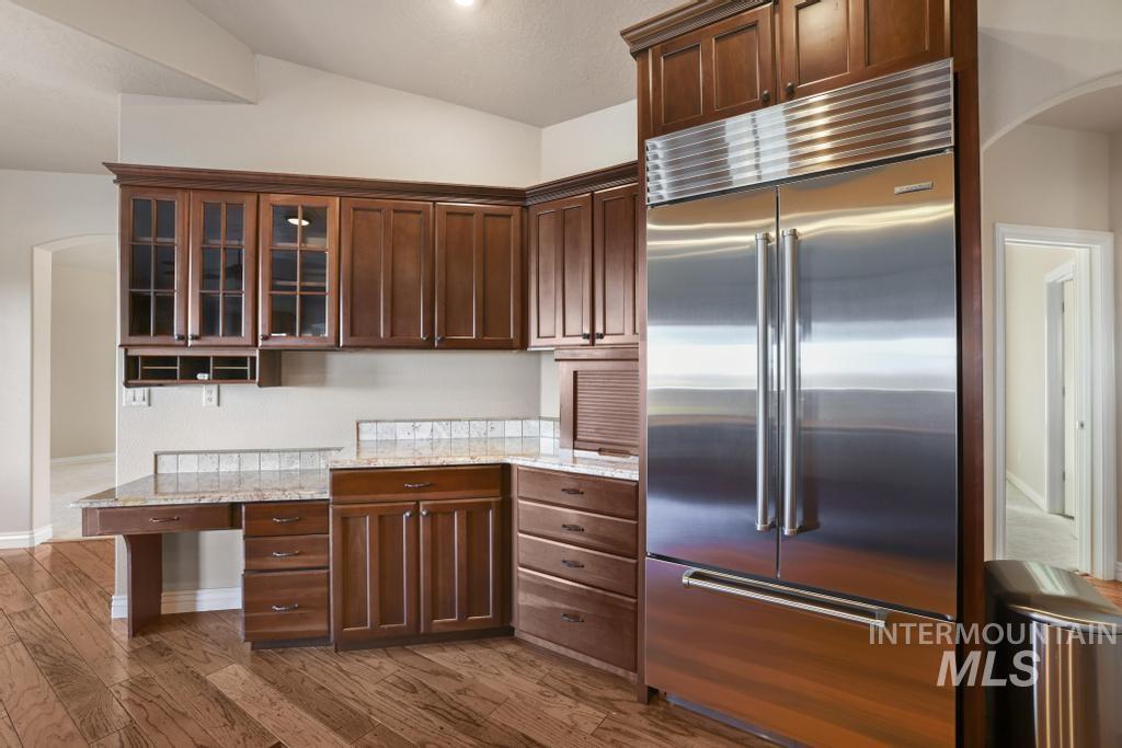 Kitchen featuring arched walkways, built in refrigerator, glass insert cabinets, light stone counters, and dark wood-style floors