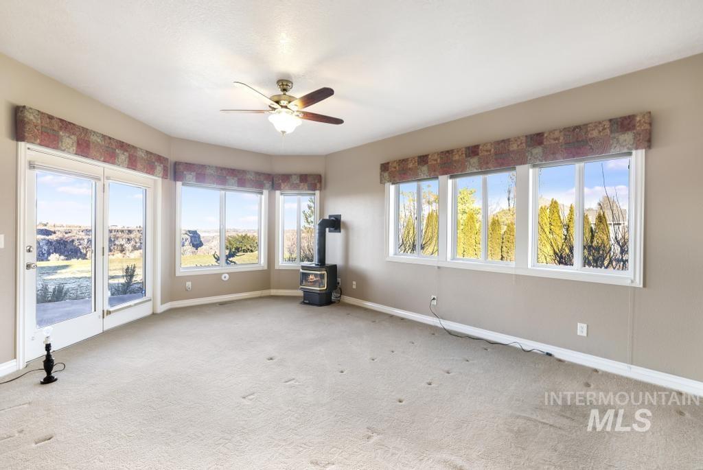 Carpeted spare room with a wood stove, a ceiling fan, and plenty of natural light