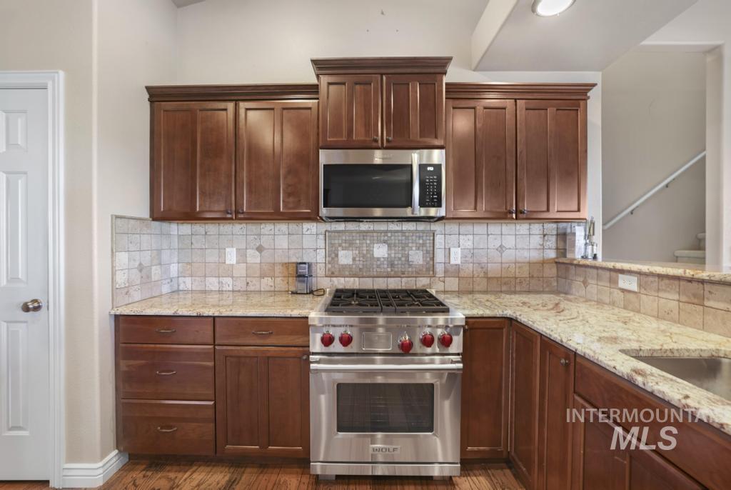 Kitchen featuring stainless steel appliances, light stone countertops, backsplash, and dark wood-type flooring