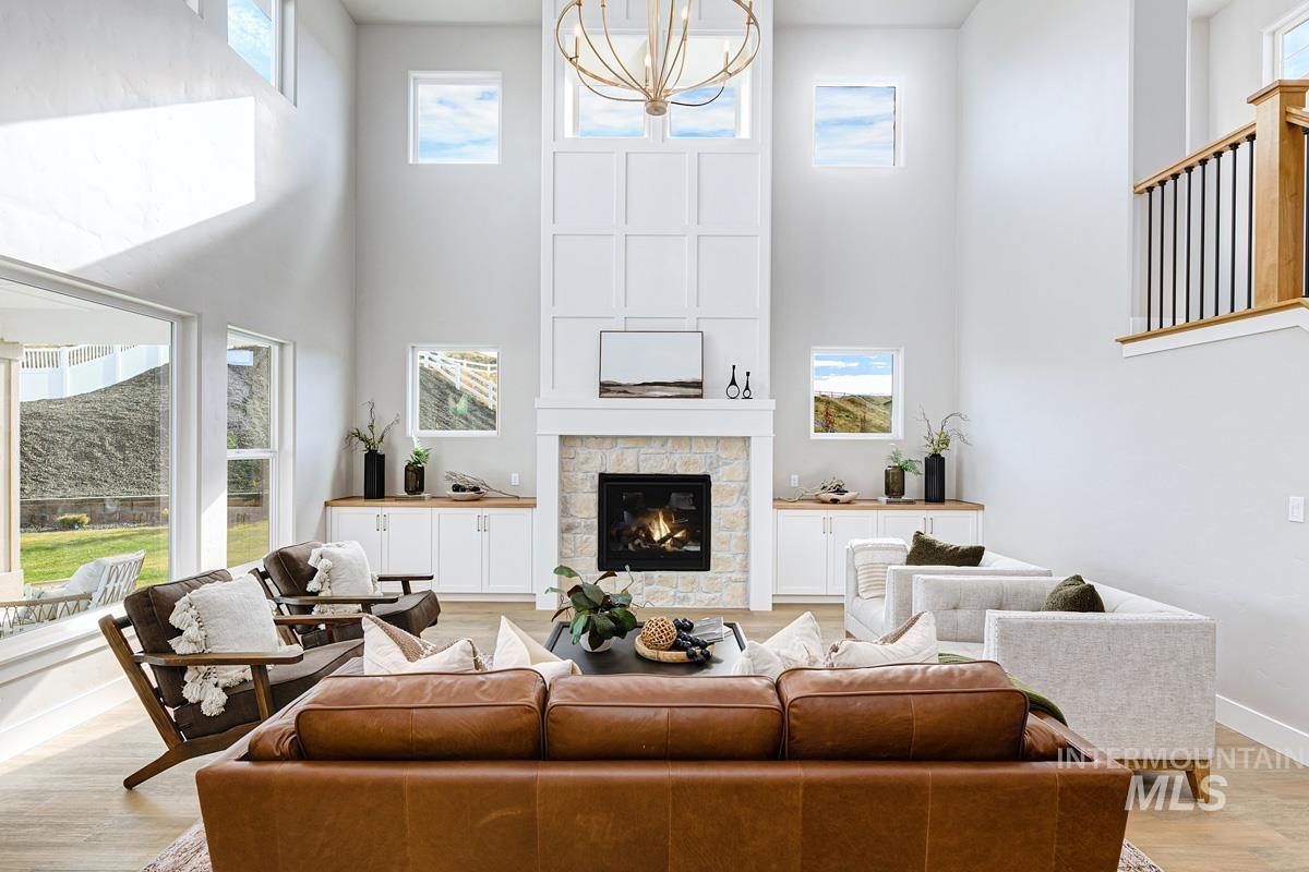 Living room featuring light wood finished floors, healthy amount of natural light, a towering ceiling, a fireplace, and a chandelier