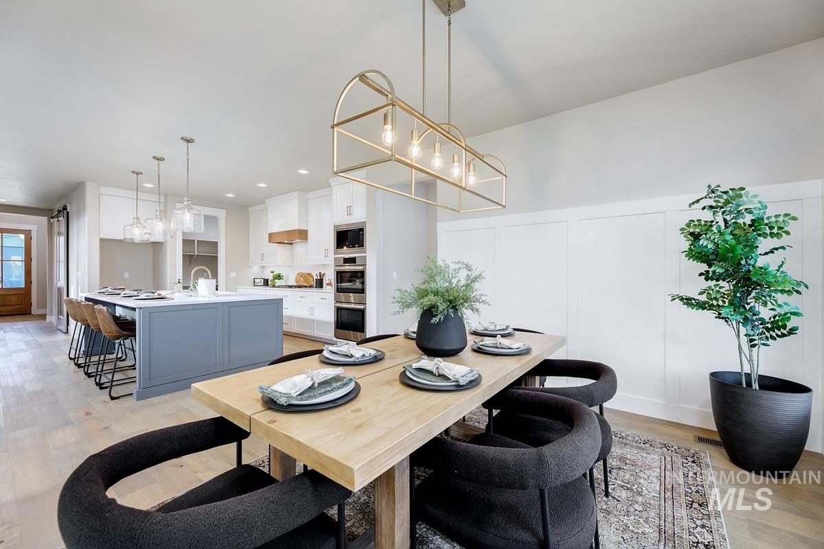 Dining room with light wood finished floors, a decorative wall, wainscoting, and recessed lighting