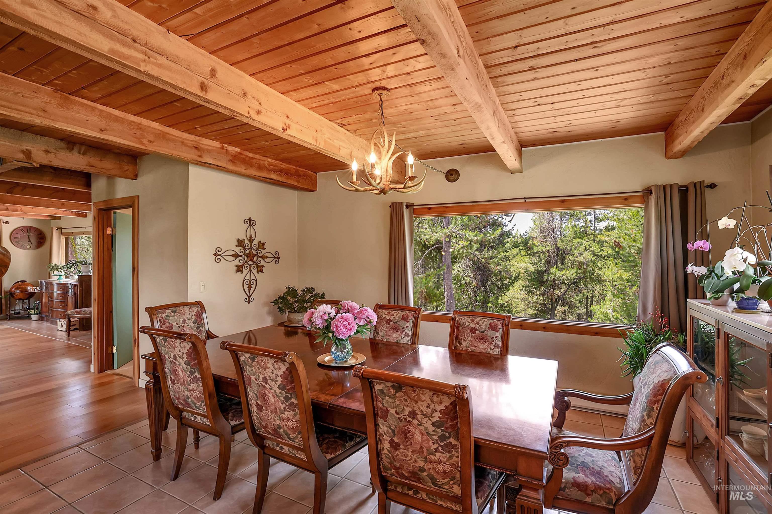 Tiled dining room with a wood ceiling with exposed beams, a chandelier, and plenty of natural light