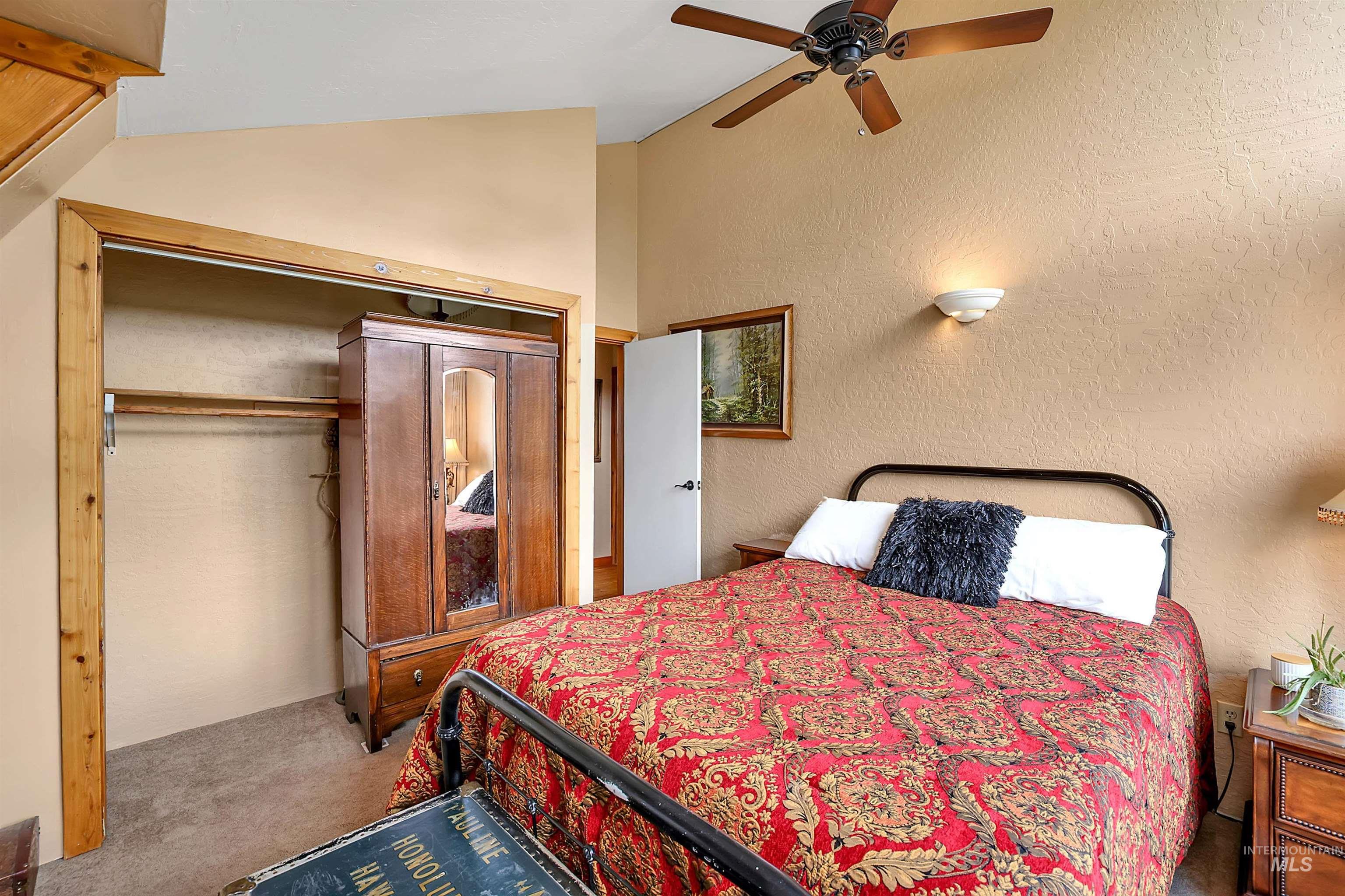 Carpeted bedroom featuring lofted ceiling, a ceiling fan, a textured wall, and a closet