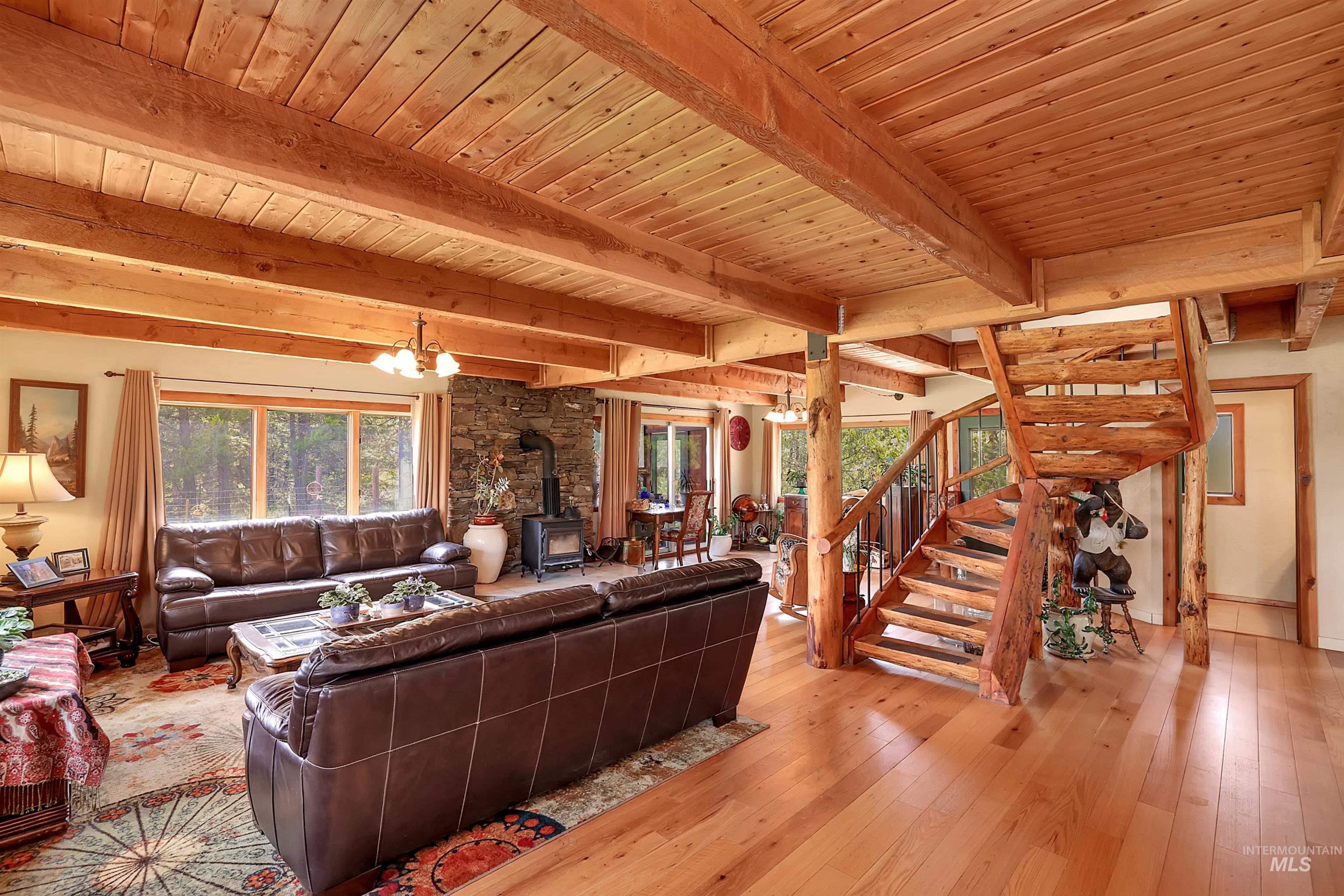 Living room with a wood stove, wood-type flooring, a chandelier, stairway, and a wood ceiling with exposed beams