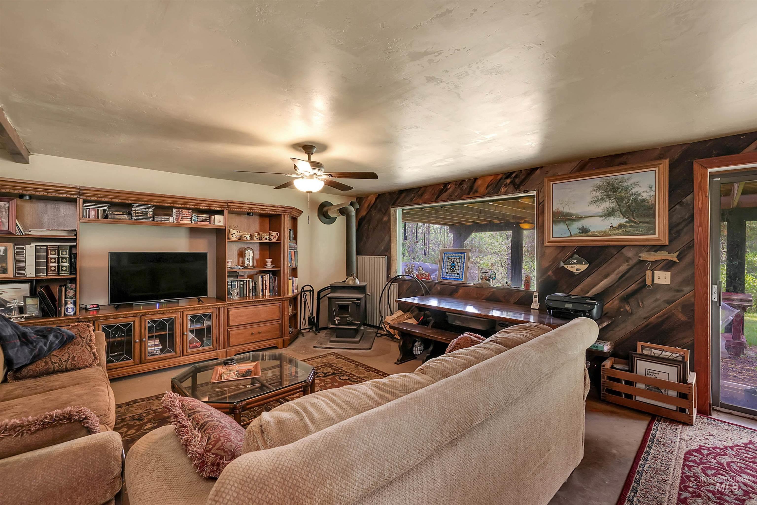 Living room with a wood stove, wooden walls, healthy amount of natural light, ceiling fan, and carpet floors