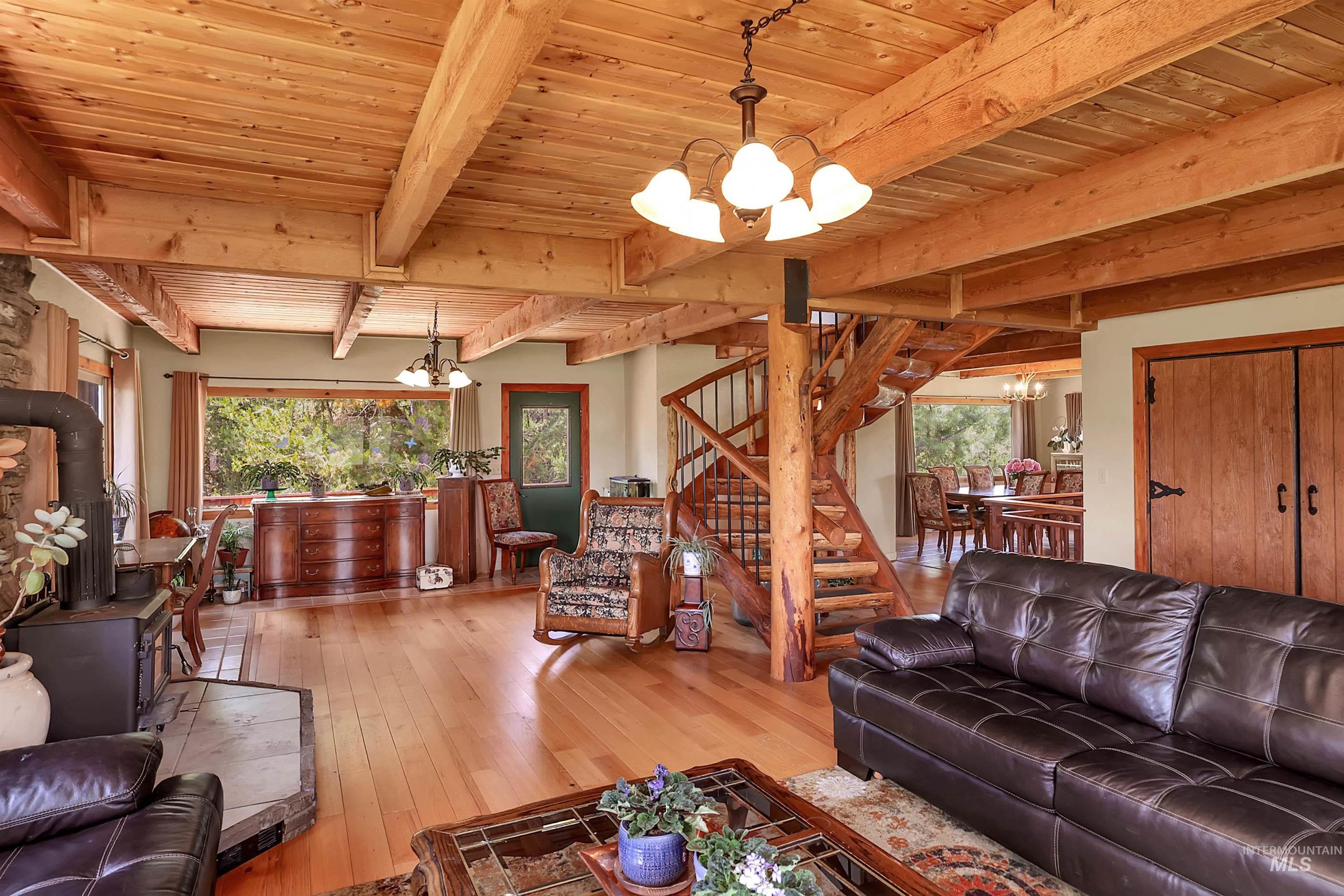 Living area featuring a chandelier, a wooden ceiling with exposed beams, a wood stove, hardwood / wood-style floors, and stairway