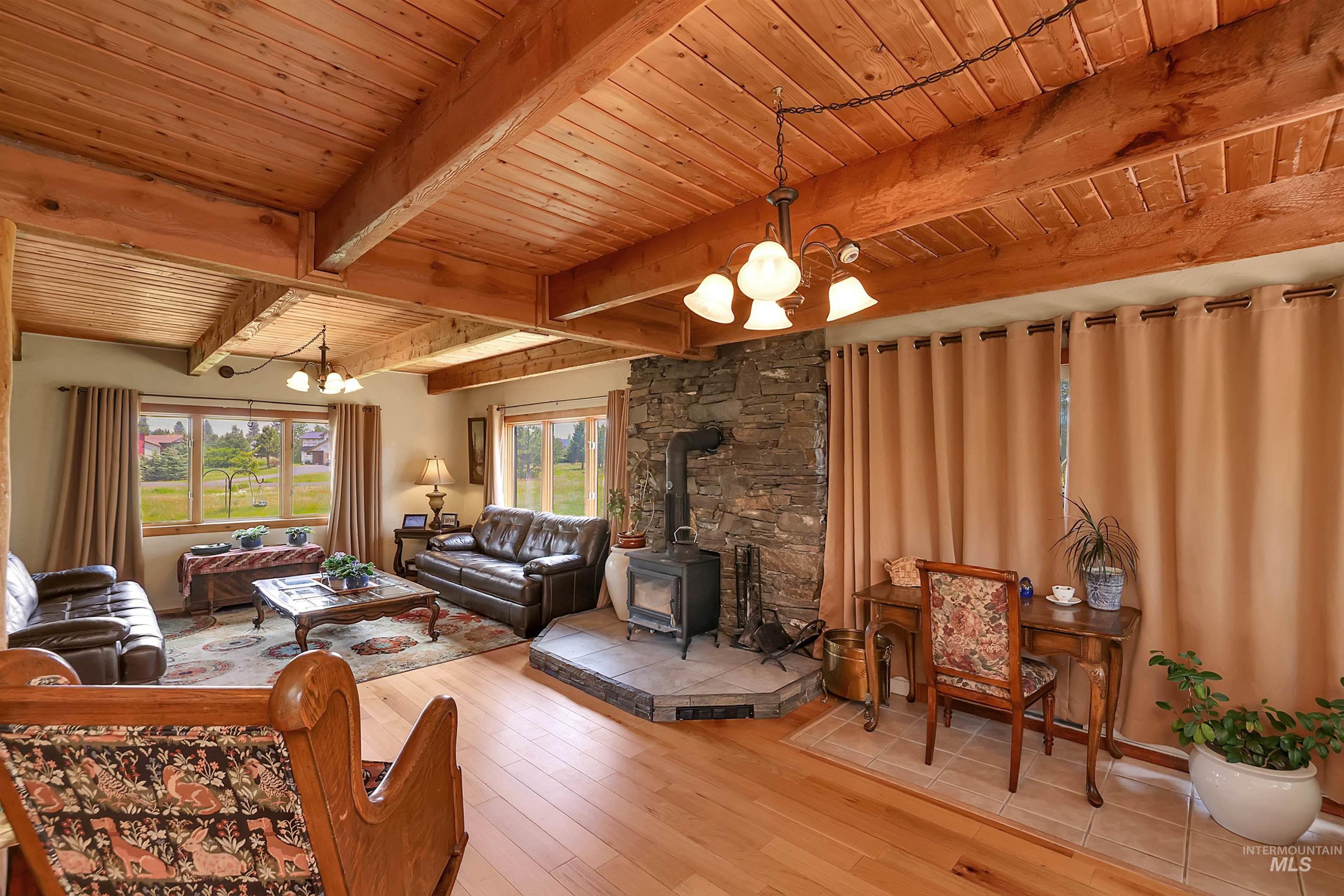 Living area with a chandelier, a wood stove, a wooden ceiling with exposed beams, and wood-type flooring