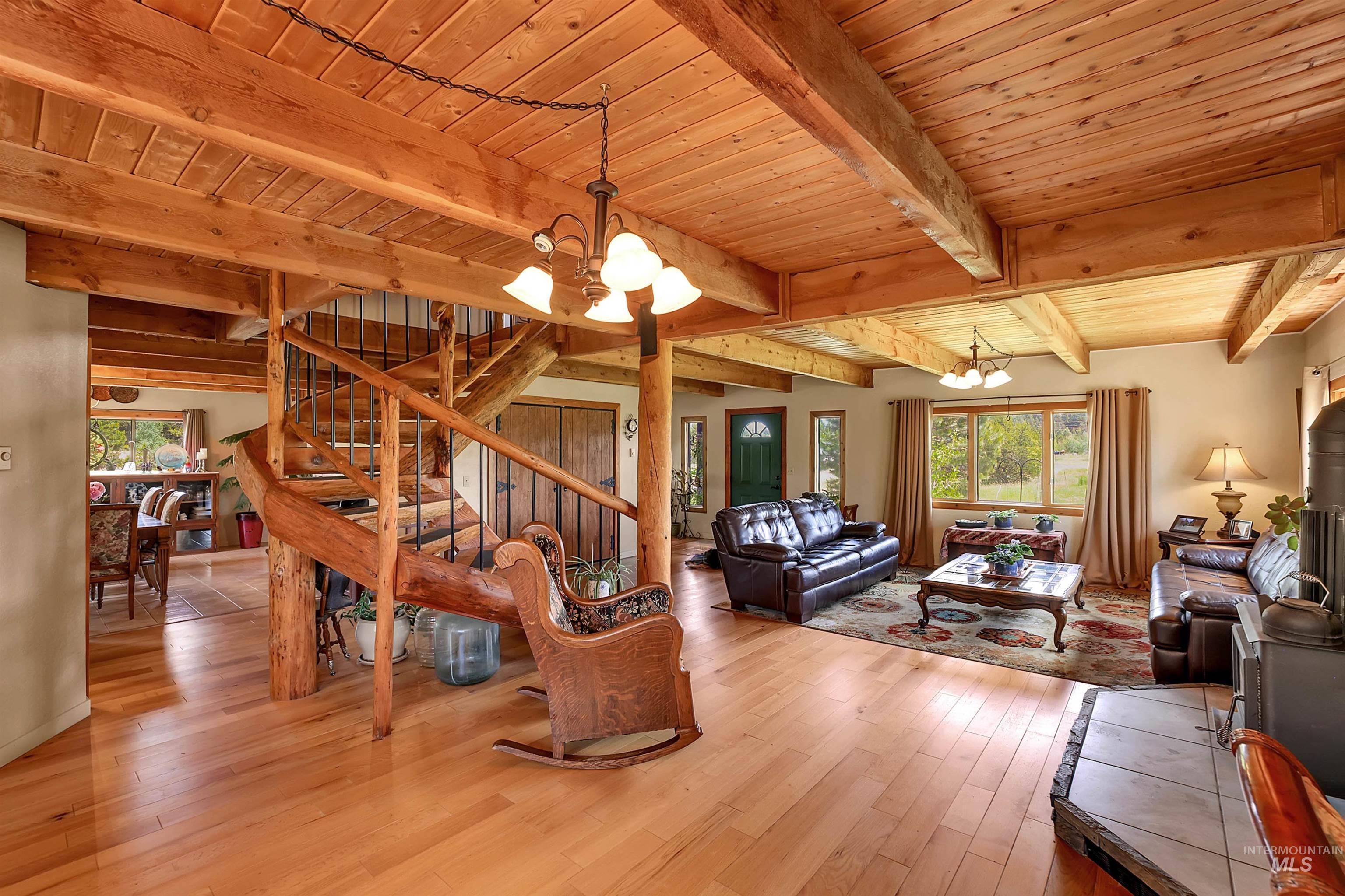 Living room with a chandelier, plenty of natural light, light wood-style floors, and a wood ceiling with exposed beams