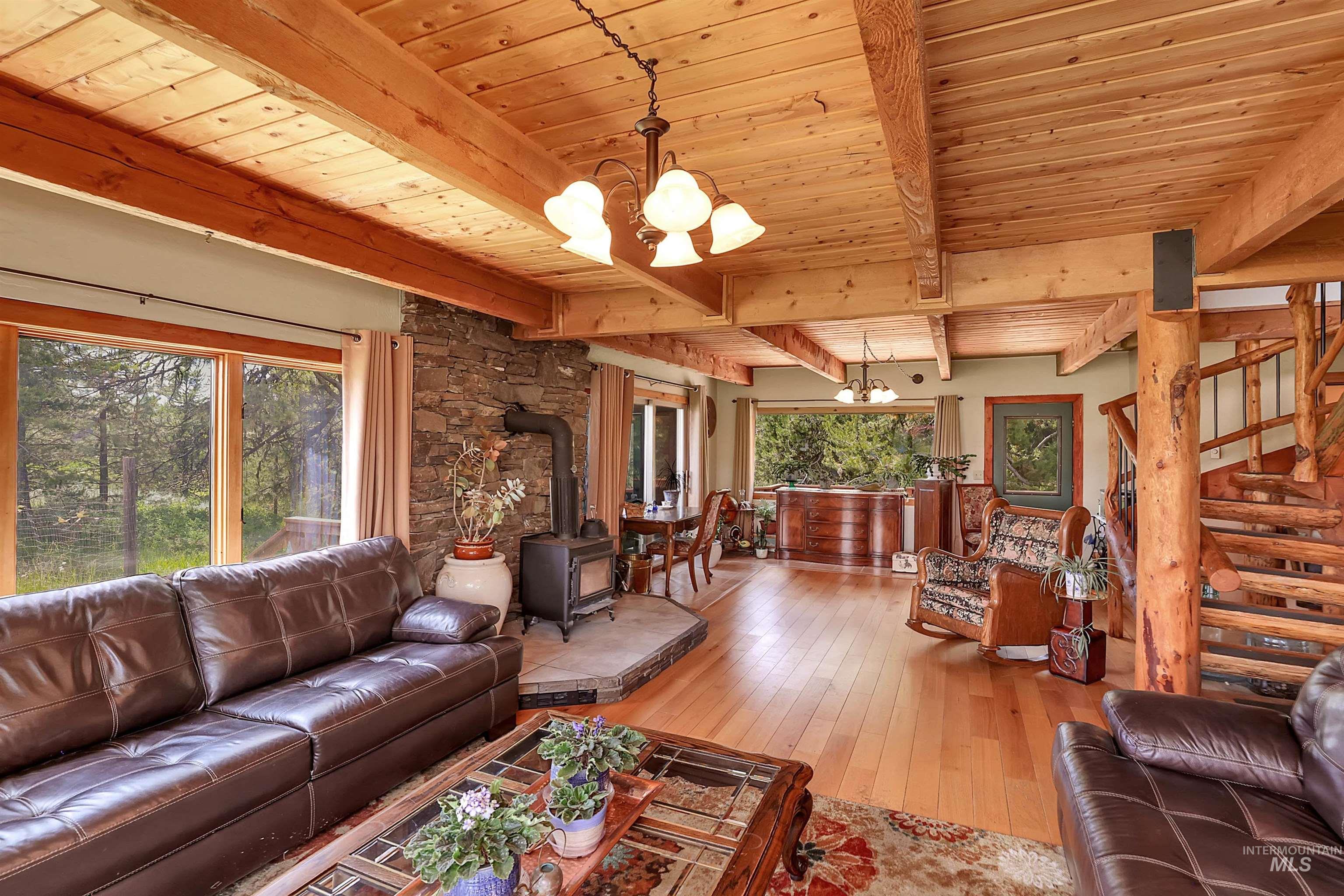 Living room with a chandelier, a wood stove, a wood ceiling with exposed beams, wood-type flooring, and stairway