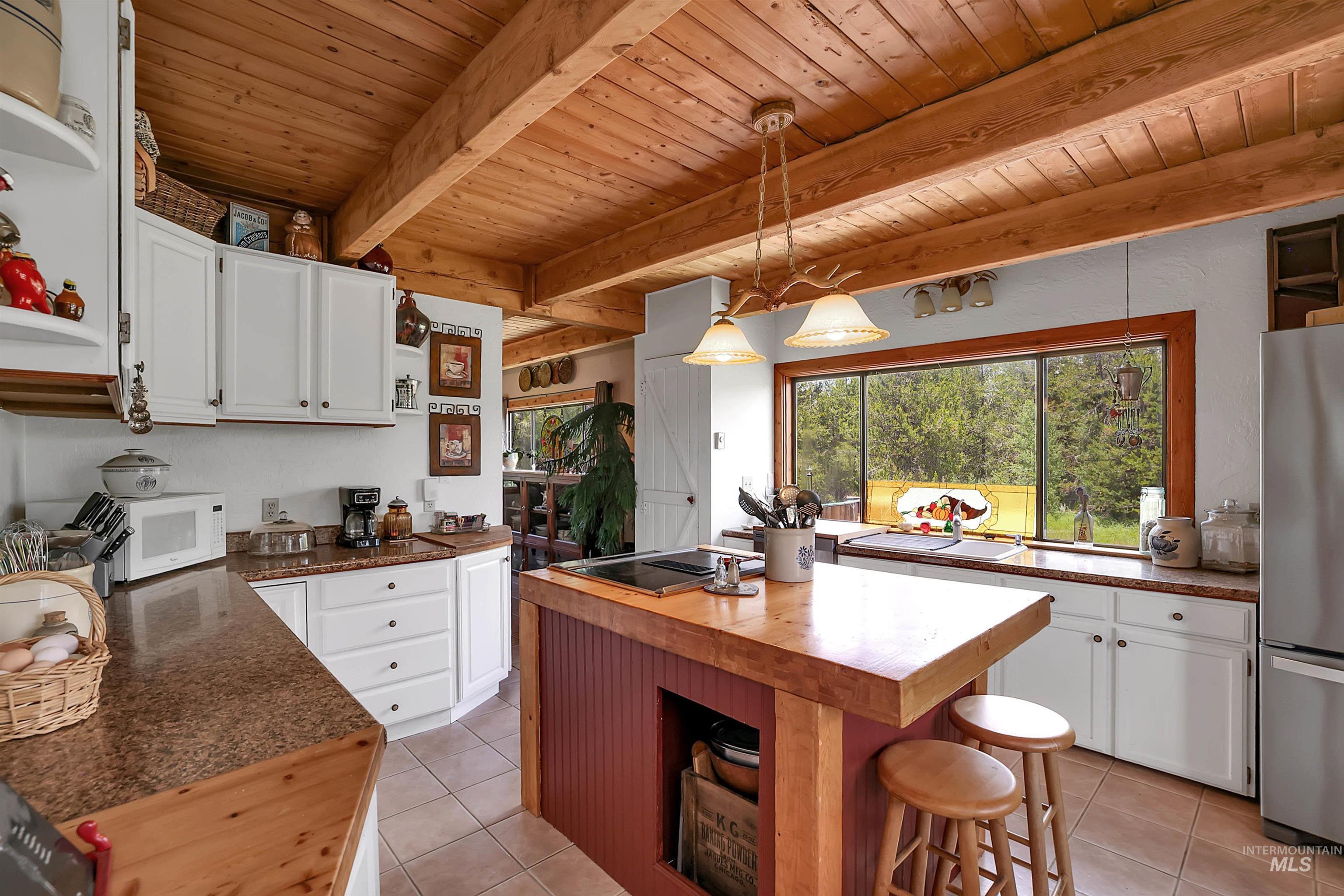 Kitchen with butcher block counters, a wooden ceiling with exposed beams, light tile patterned floors, and white cabinetry