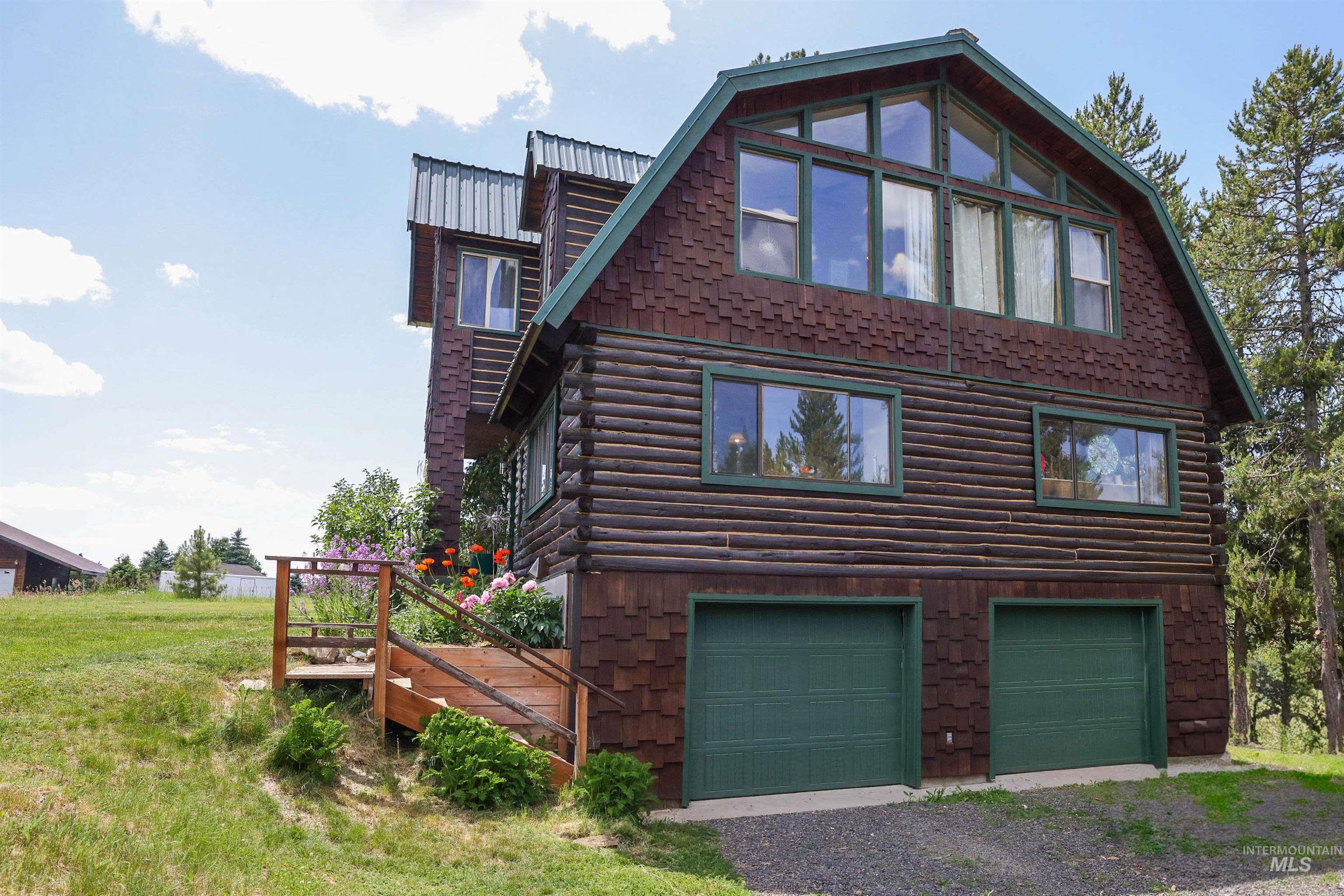 View of home's exterior with log exterior, a garage, driveway, and a gambrel roof