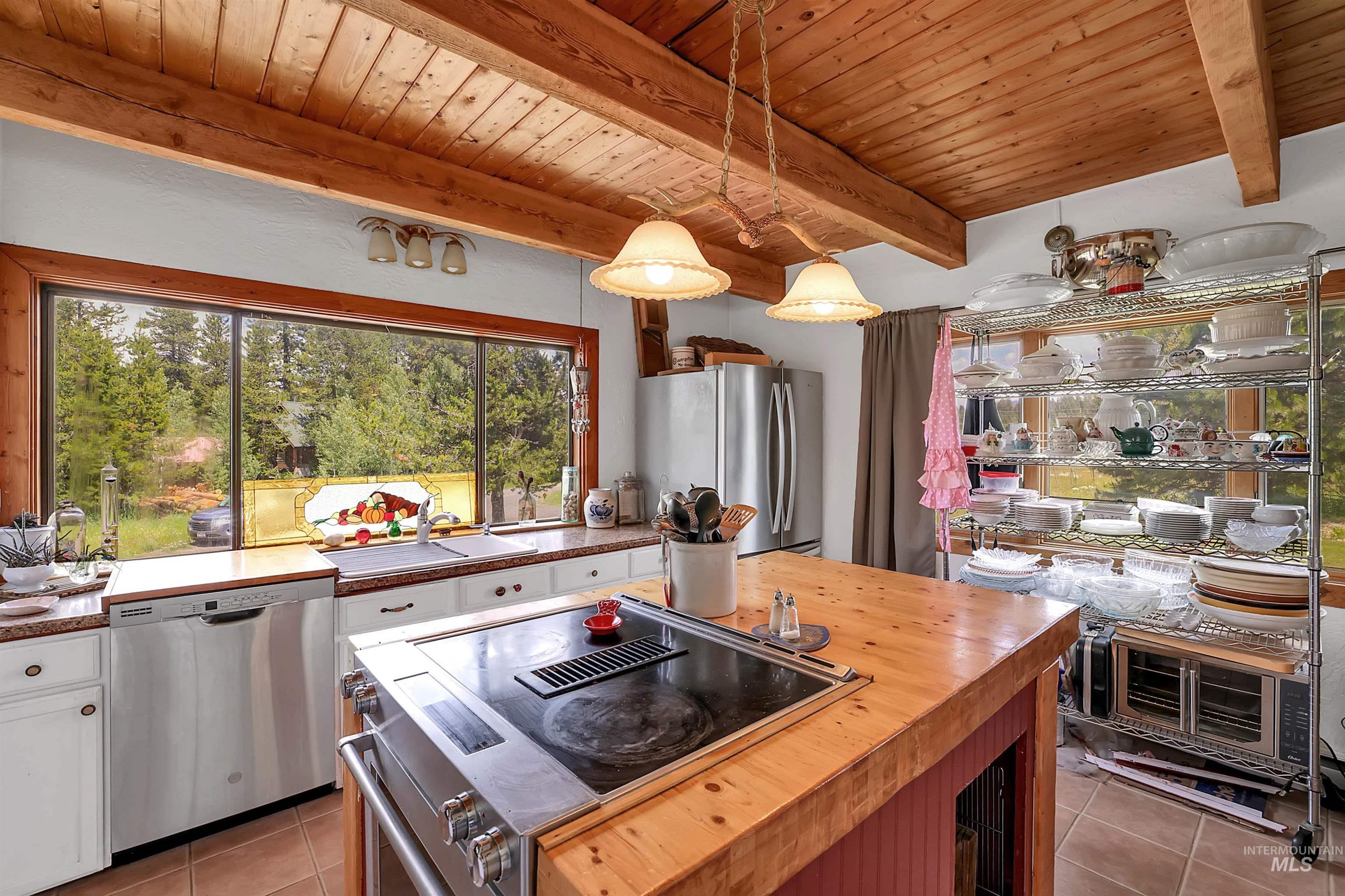 Kitchen with wood counters, light tile patterned flooring, stainless steel appliances, a wooden ceiling with exposed beams, and white cabinets
