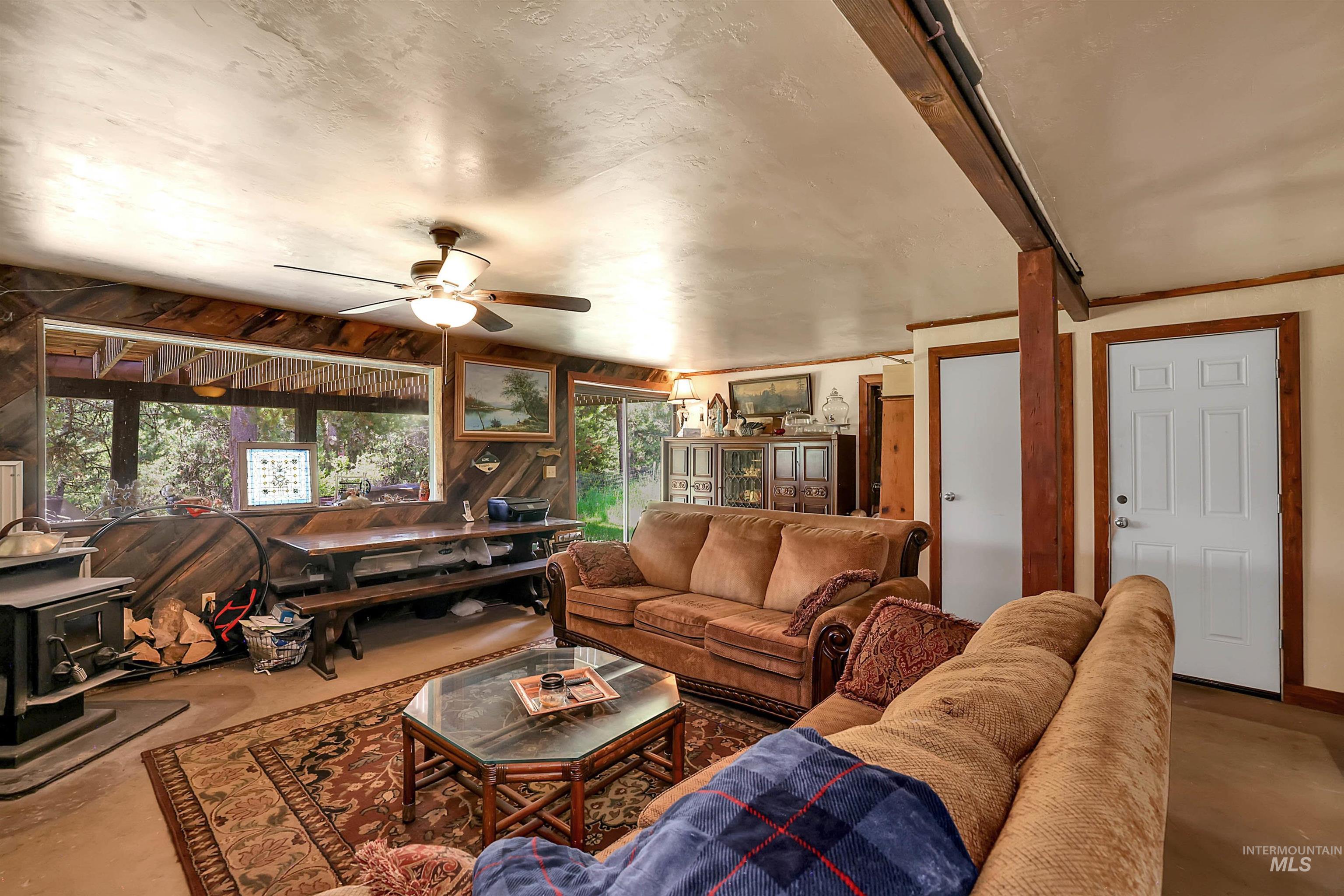 Living area with a wood stove, a ceiling fan, and concrete floors
