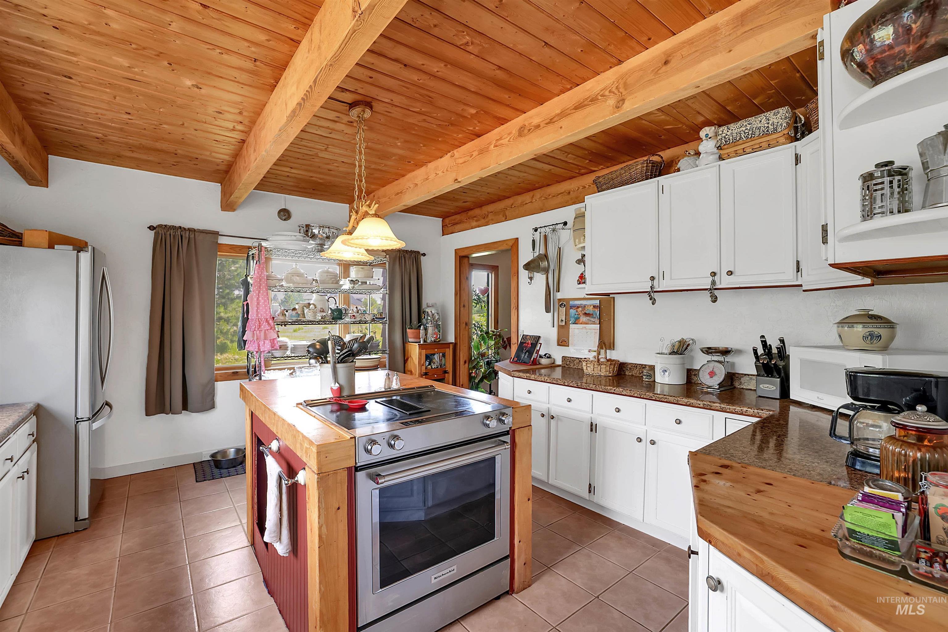 Kitchen with butcher block counters, appliances with stainless steel finishes, healthy amount of natural light, and a wood ceiling with exposed beams