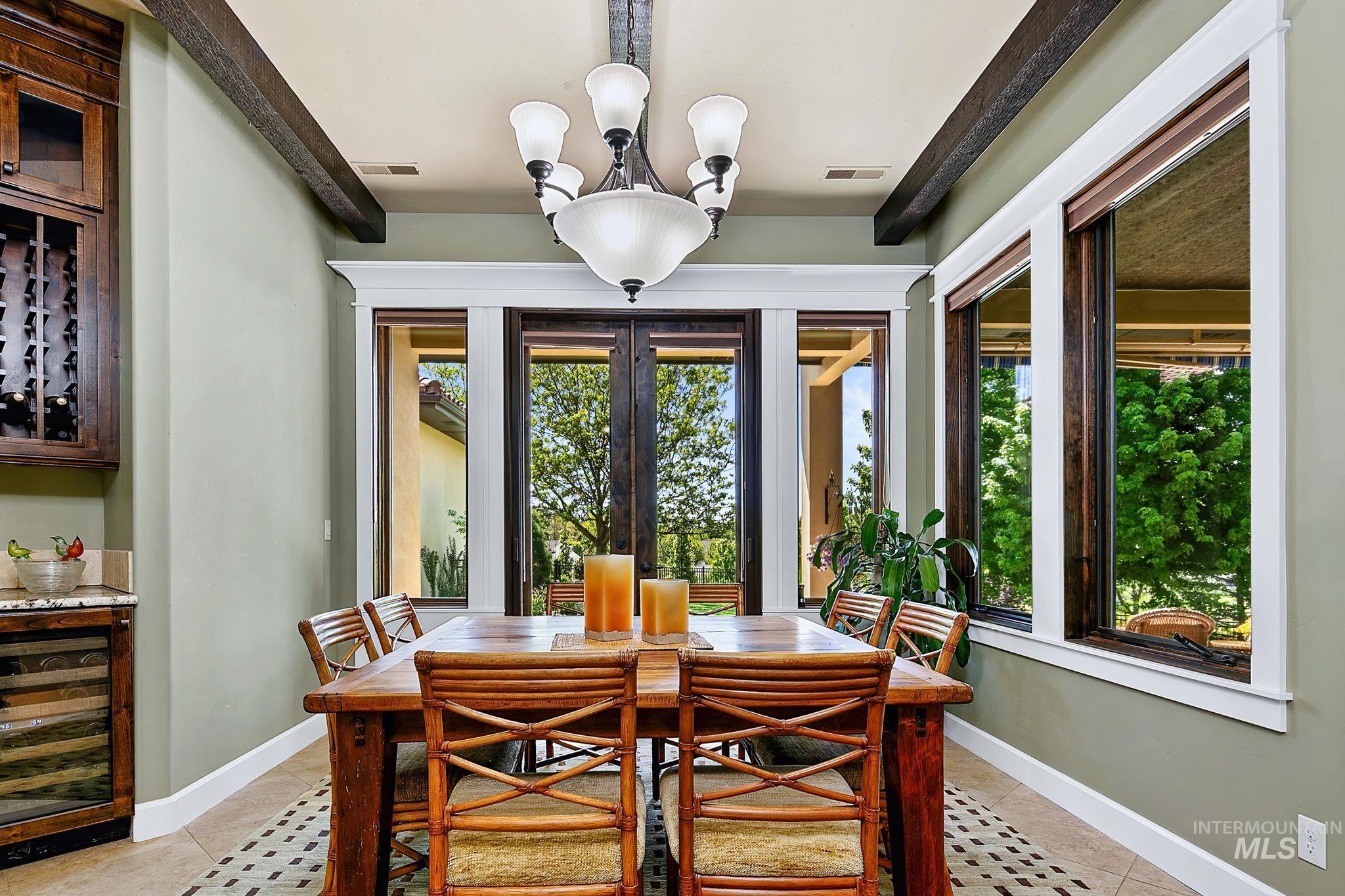 Formal dining space featuring beam-accented ceilings, a built-in wine fridge, and abundant natural light