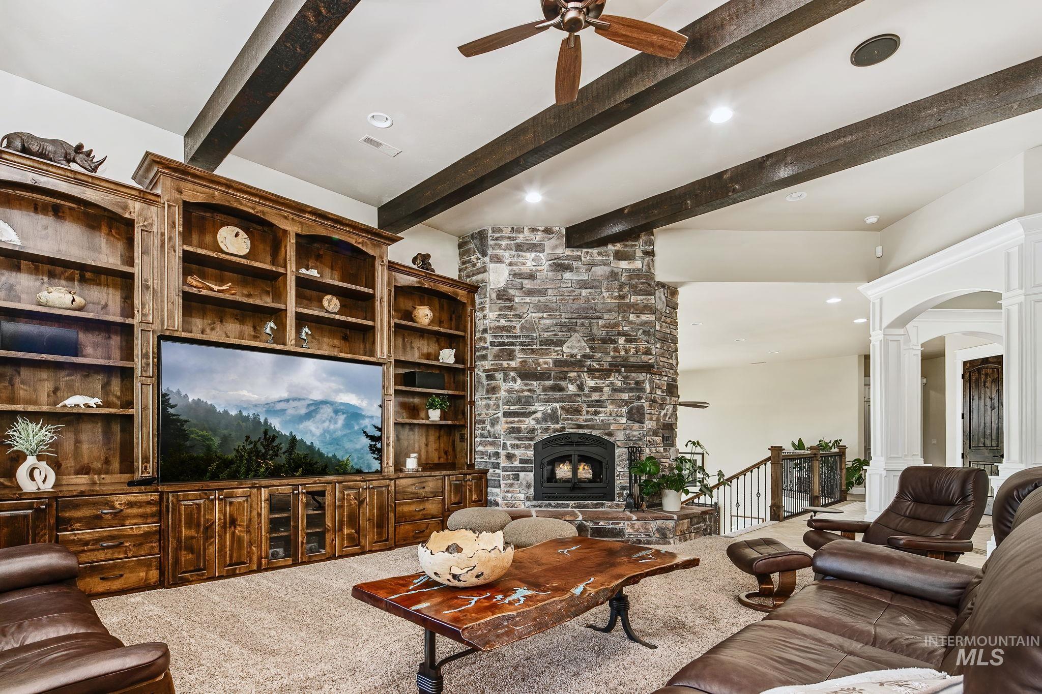 Statement great room showcasing exposed wood beams, custom millwork, and an impressive stone hearth centerpiece