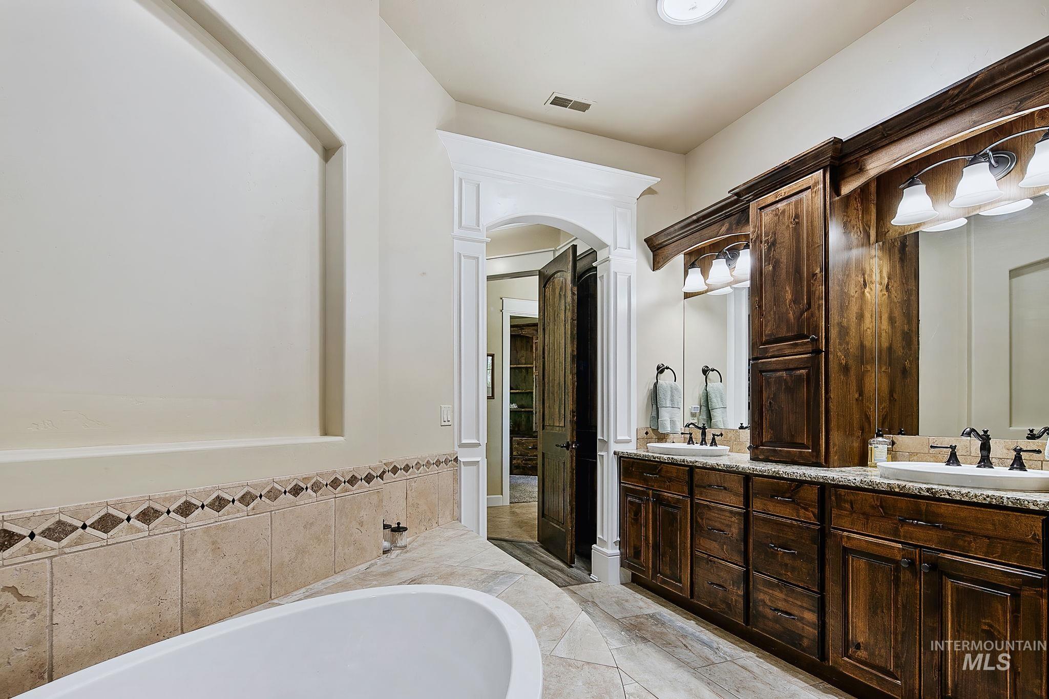 Luxurious primary bath with granite countertops, custom wood cabinetry, and a relaxing soaking tub