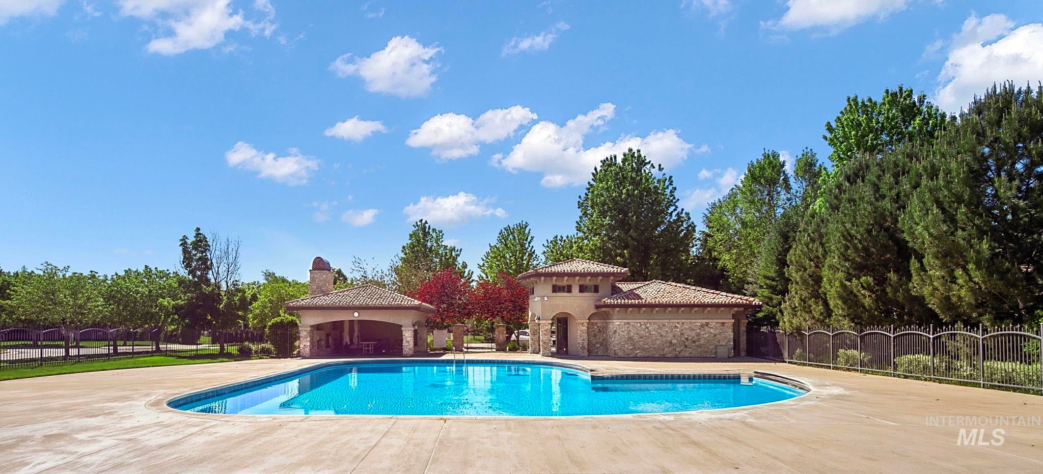 Resort-style community pool featuring expansive patio space, beautifully maintained grounds, and a poolside clubhouse pavilion surrounded by mature trees