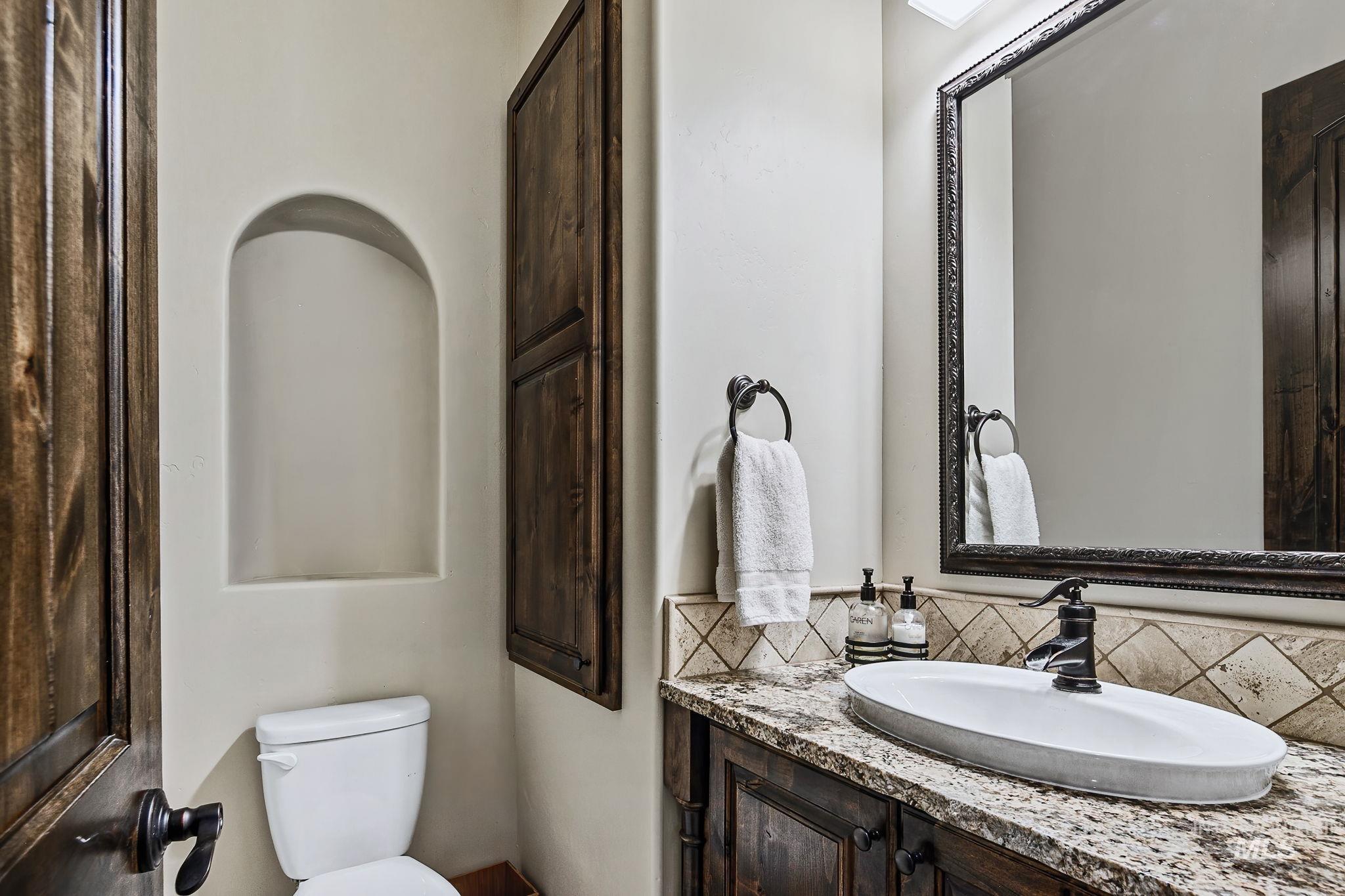 Elegant main-level powder bath featuring granite countertops, custom wood cabinetry, and upscale finishes