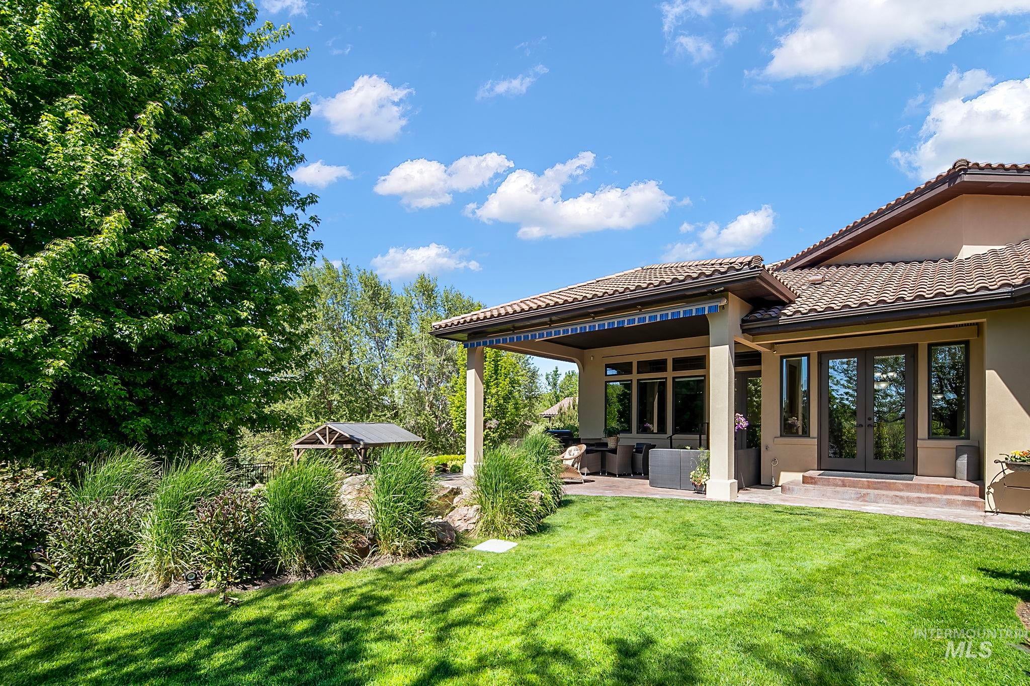 Resort-style backyard retreat featuring a covered patio, outdoor kitchen, lush landscaping, and mature trees. Perfect for relaxing or entertaining in a private setting