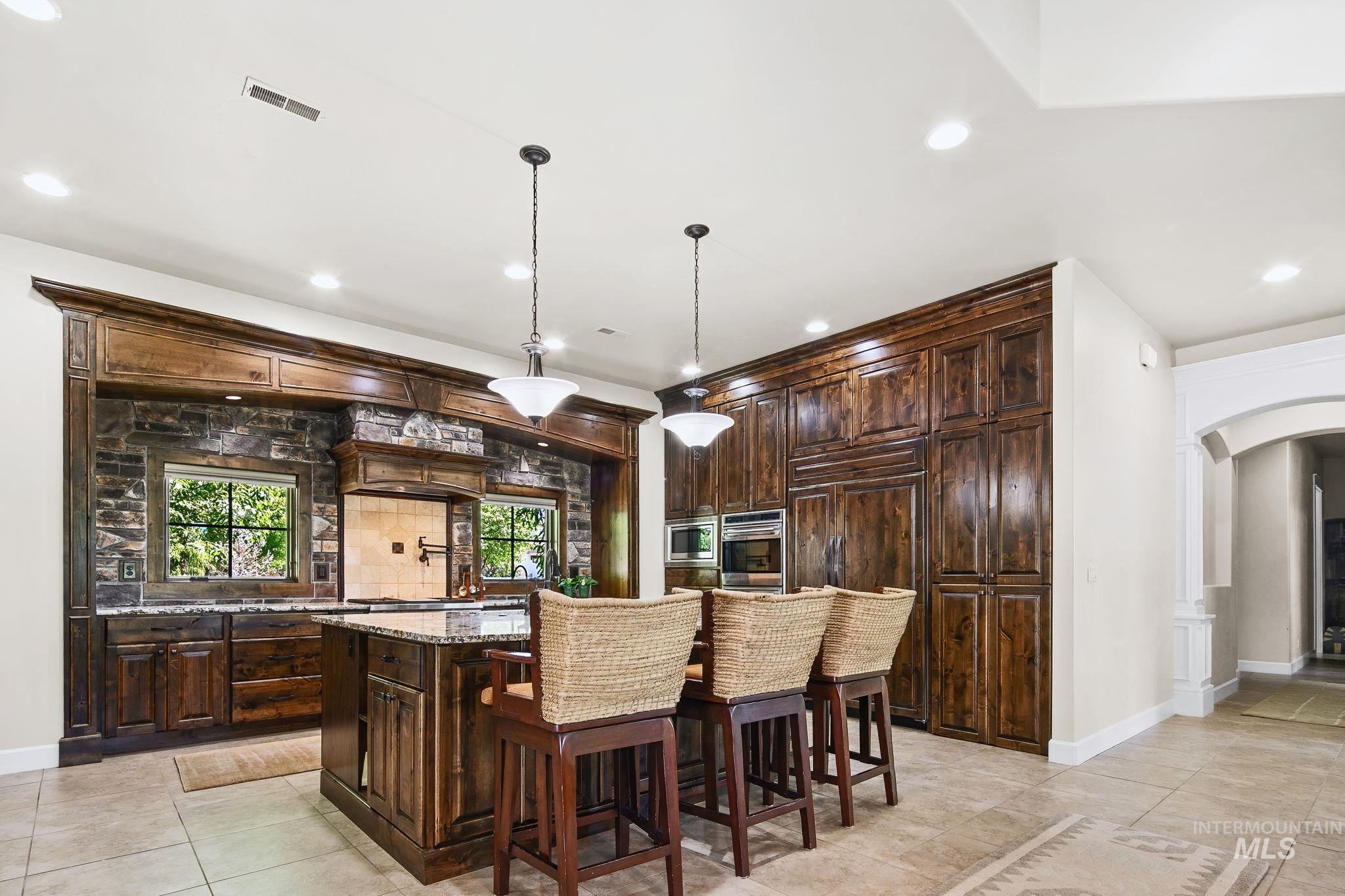 Chef?s kitchen featuring rich custom cabinetry, oversized island seating, and stunning stone accents