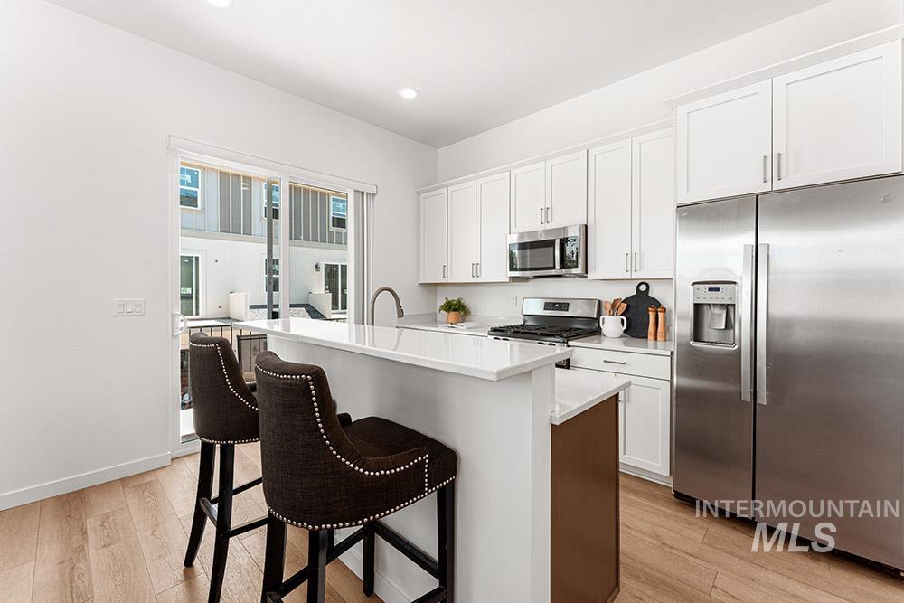 Kitchen featuring stainless steel appliances, white cabinets, an island with sink, light wood-style floors, and a kitchen breakfast bar