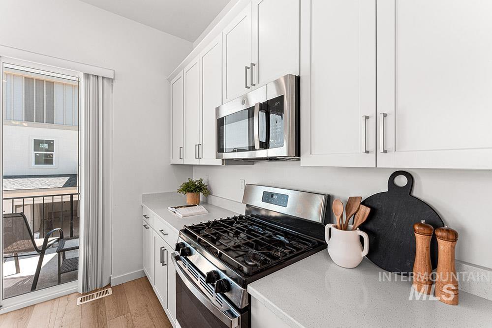 Kitchen with stainless steel appliances, white cabinetry, light wood finished floors, and light stone counters