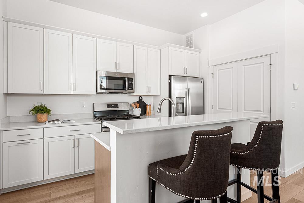 Kitchen featuring white cabinets, stainless steel appliances, an island with sink, light wood-style flooring, and recessed lighting