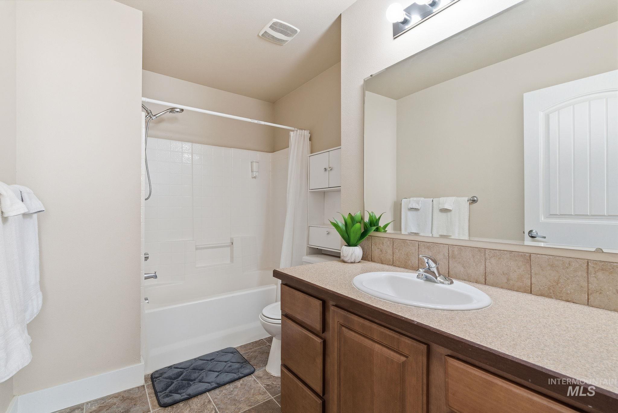 Bathroom with shower / bathtub combination with curtain, vanity, and dark tile patterned flooring