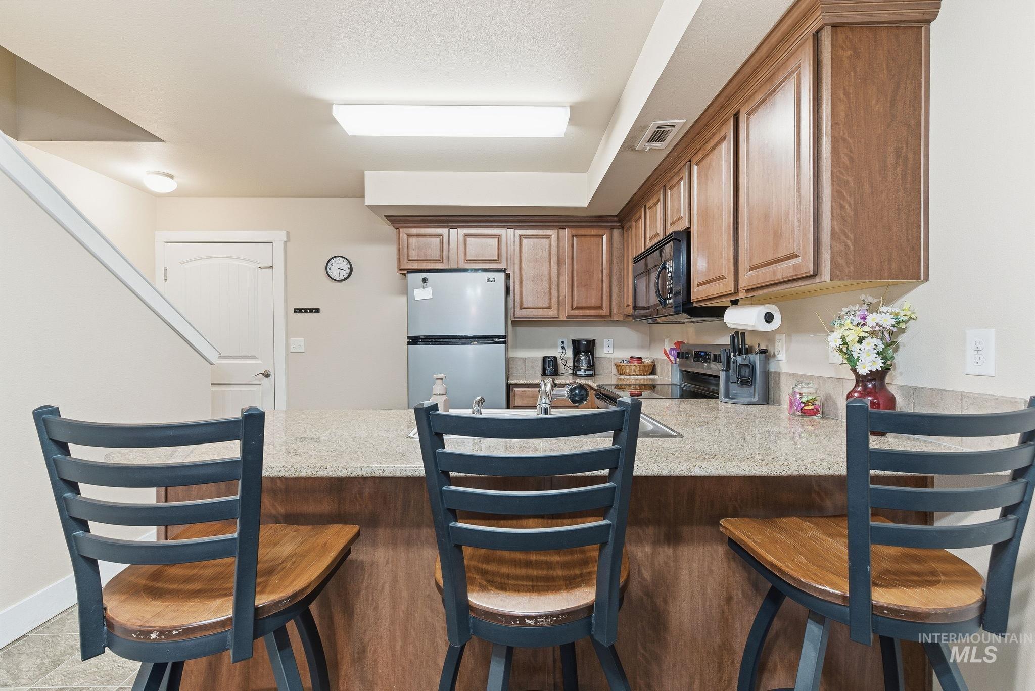 Kitchen featuring a kitchen bar, a peninsula, stainless steel appliances, and light stone counters