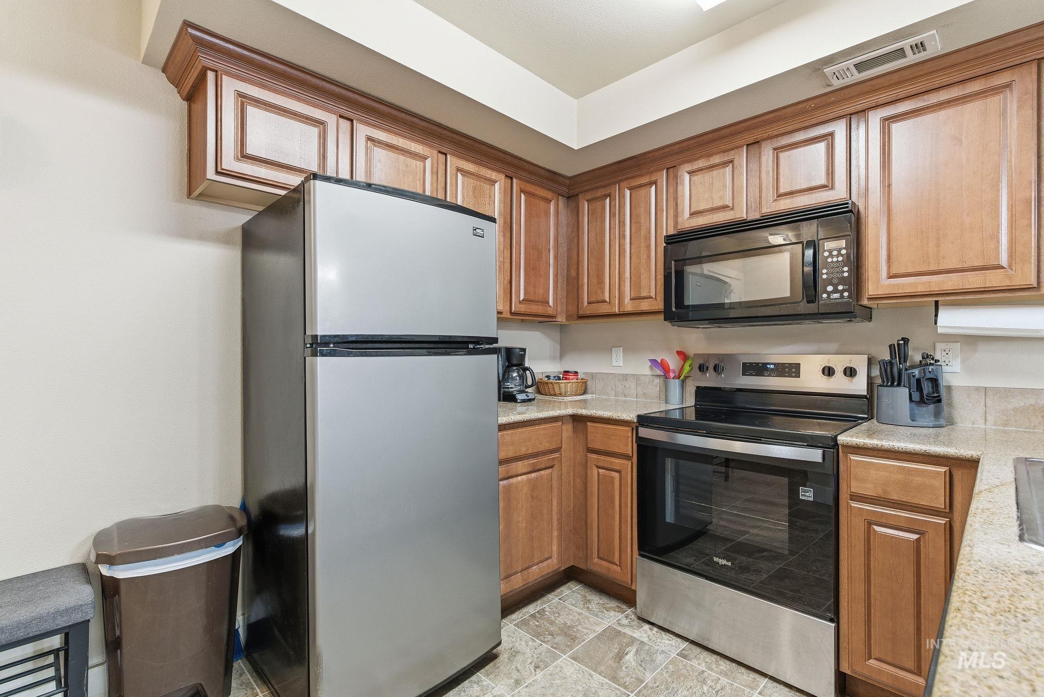 Kitchen featuring appliances with stainless steel finishes, brown cabinets, light stone counters, and stone finish floors