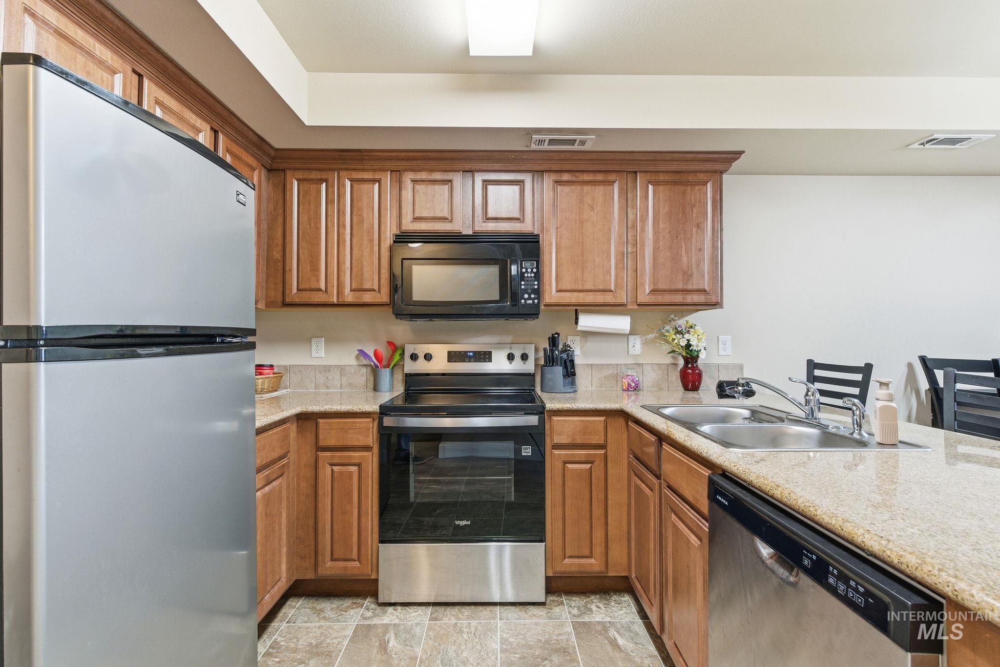 Kitchen featuring appliances with stainless steel finishes, brown cabinets, a peninsula, and light stone counters