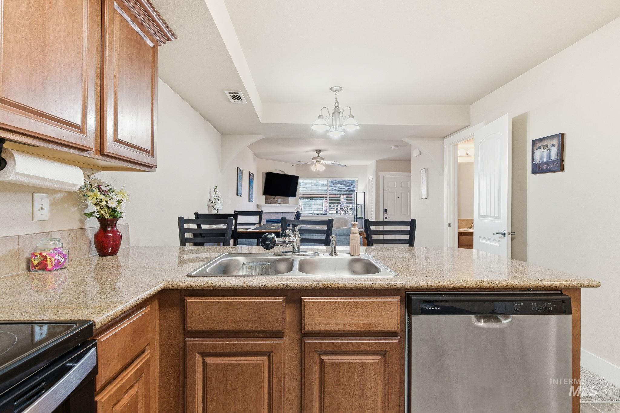 Kitchen featuring dishwasher, a peninsula, open floor plan, brown cabinetry, and a chandelier