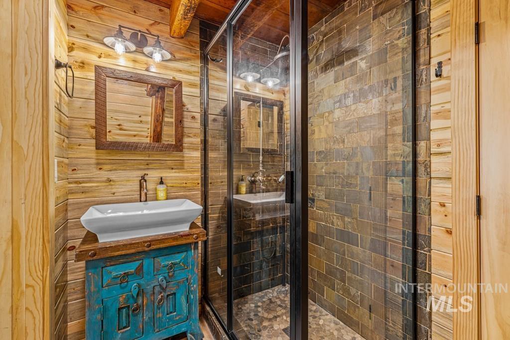 Bathroom featuring vanity, a shower stall, beam ceiling, and wooden walls