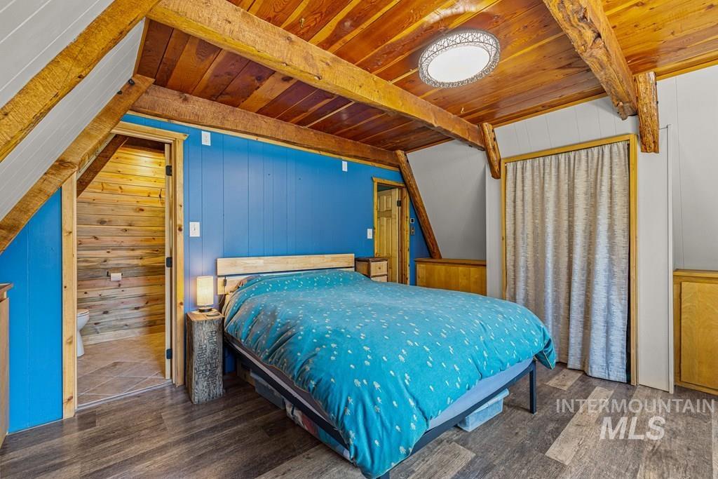 Bedroom with wooden walls, dark wood-style flooring, and a wooden ceiling with exposed beams