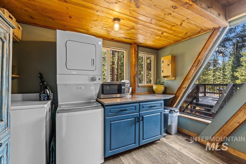 Laundry area with light wood finished floors, wood ceiling, and stacked washer and clothes dryer