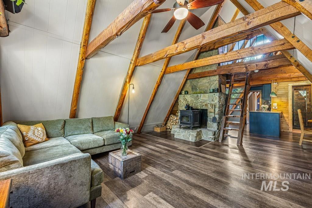Unfurnished living room with beamed ceiling, a wood stove, wood walls, wood finished floors, and high vaulted ceiling