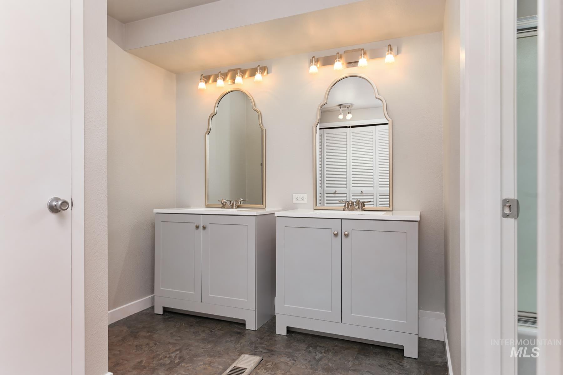 Full bathroom featuring two vanities and baseboards