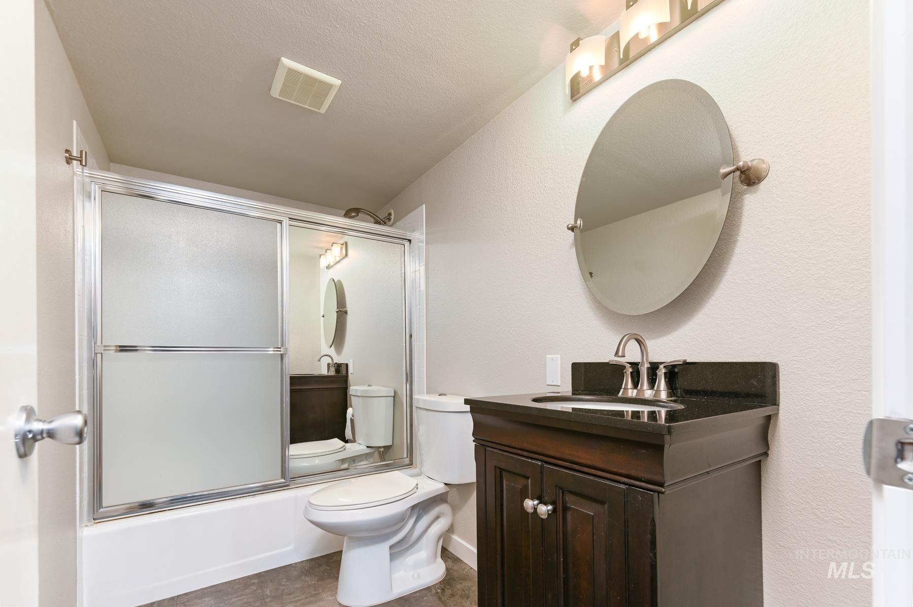 Full bath with vanity, bath / shower combo with glass door, and a textured wall