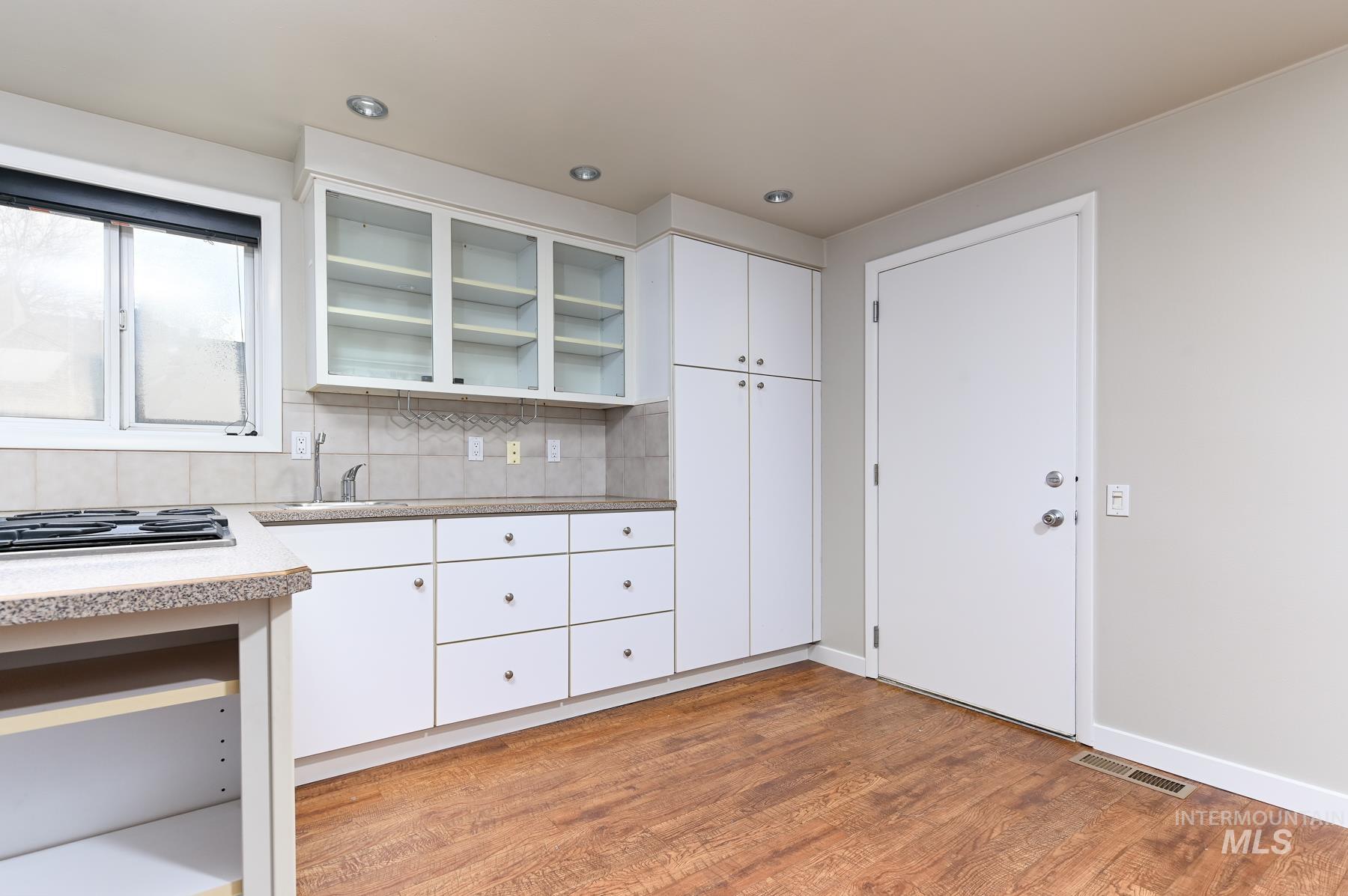 Kitchen with white cabinetry, tasteful backsplash, light wood-type flooring, and glass insert cabinets
